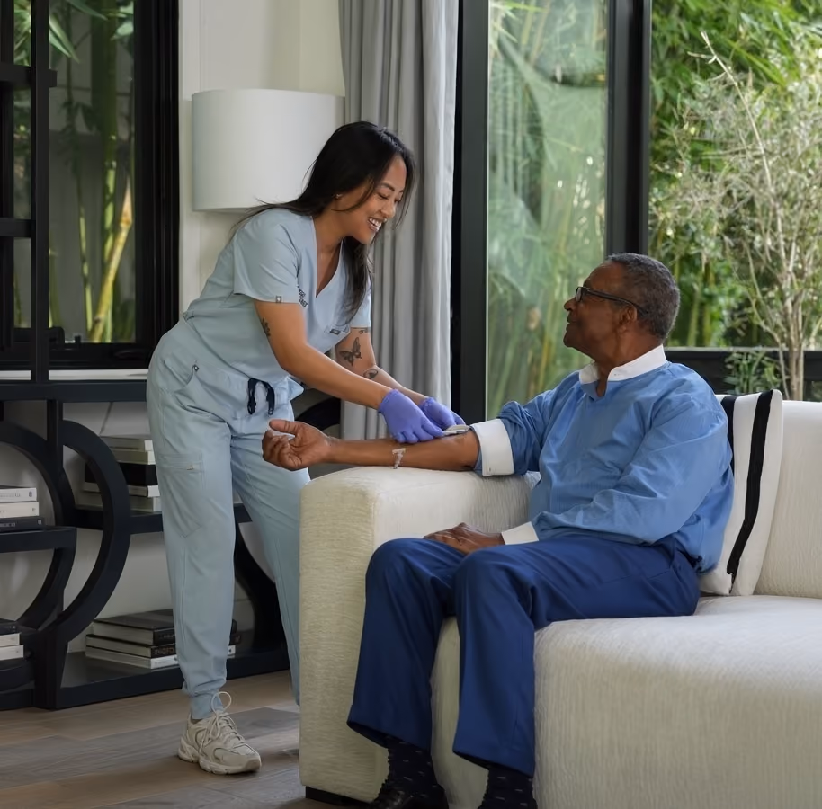 Woman administering an IV to a man in his home sitting on a couch.
