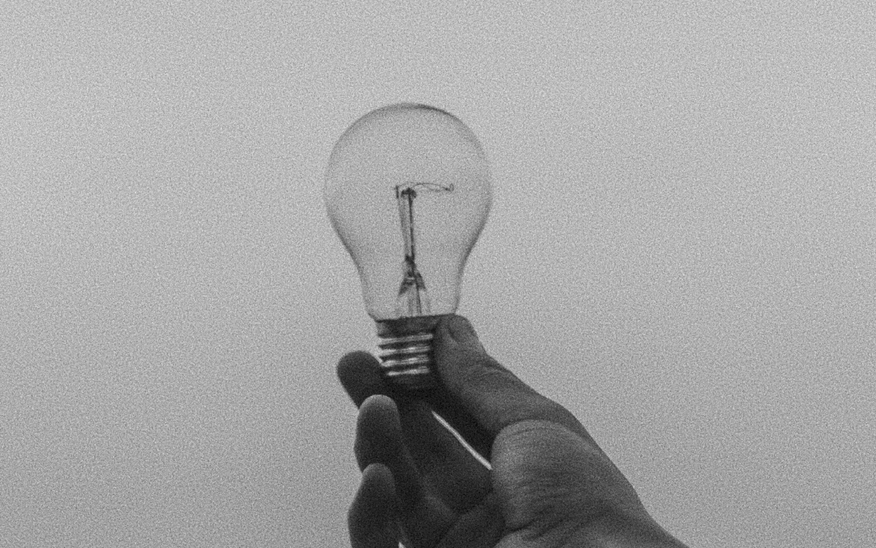 A hand holding a clear incandescent light bulb against a plain background.