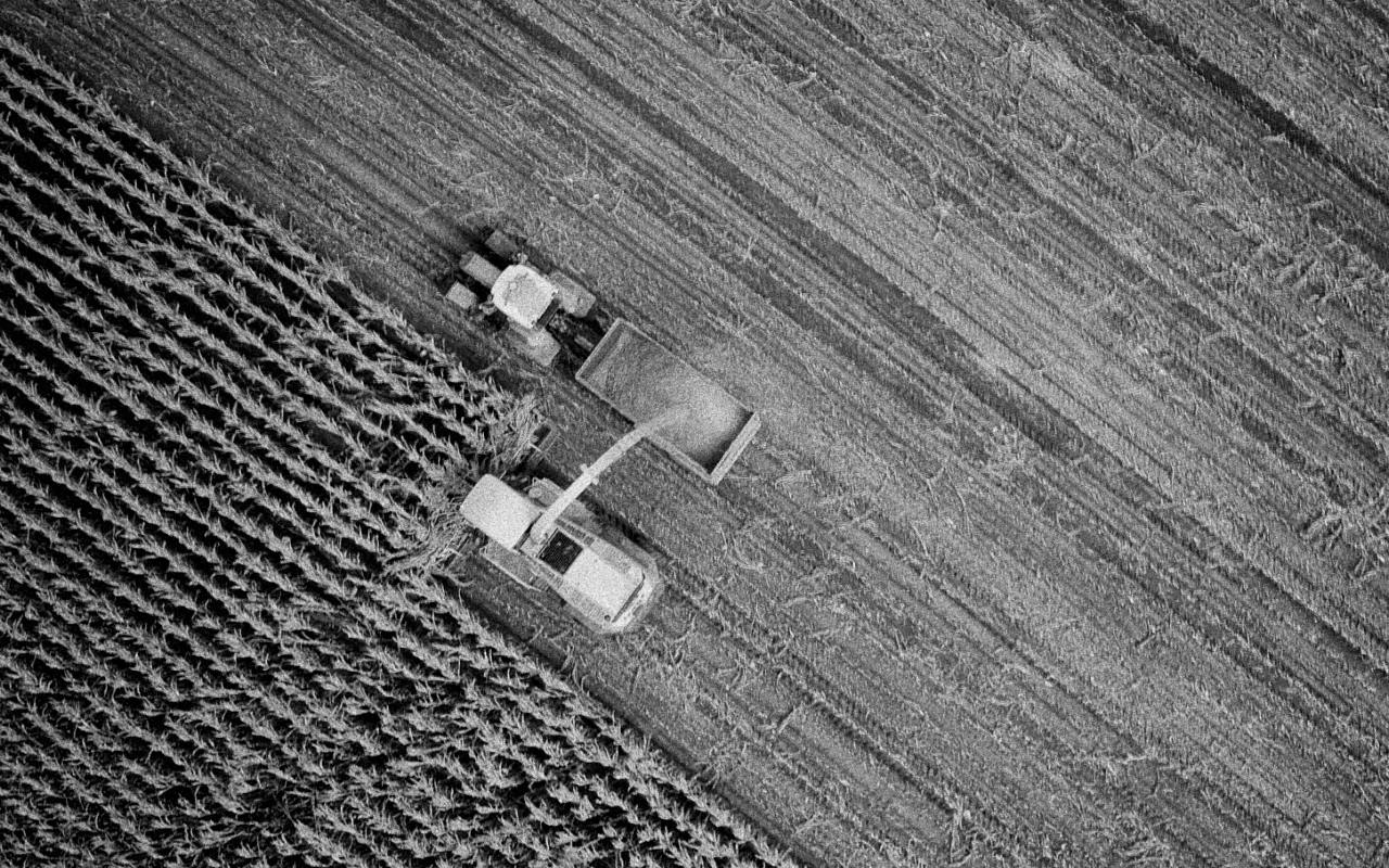 Aerial view of a combine harvester unloading corn into a tractor trailer in a harvested field.