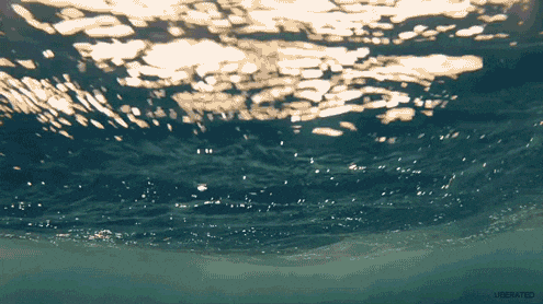 Underwater view of ocean waves with sunlight shimmering on the water's surface.