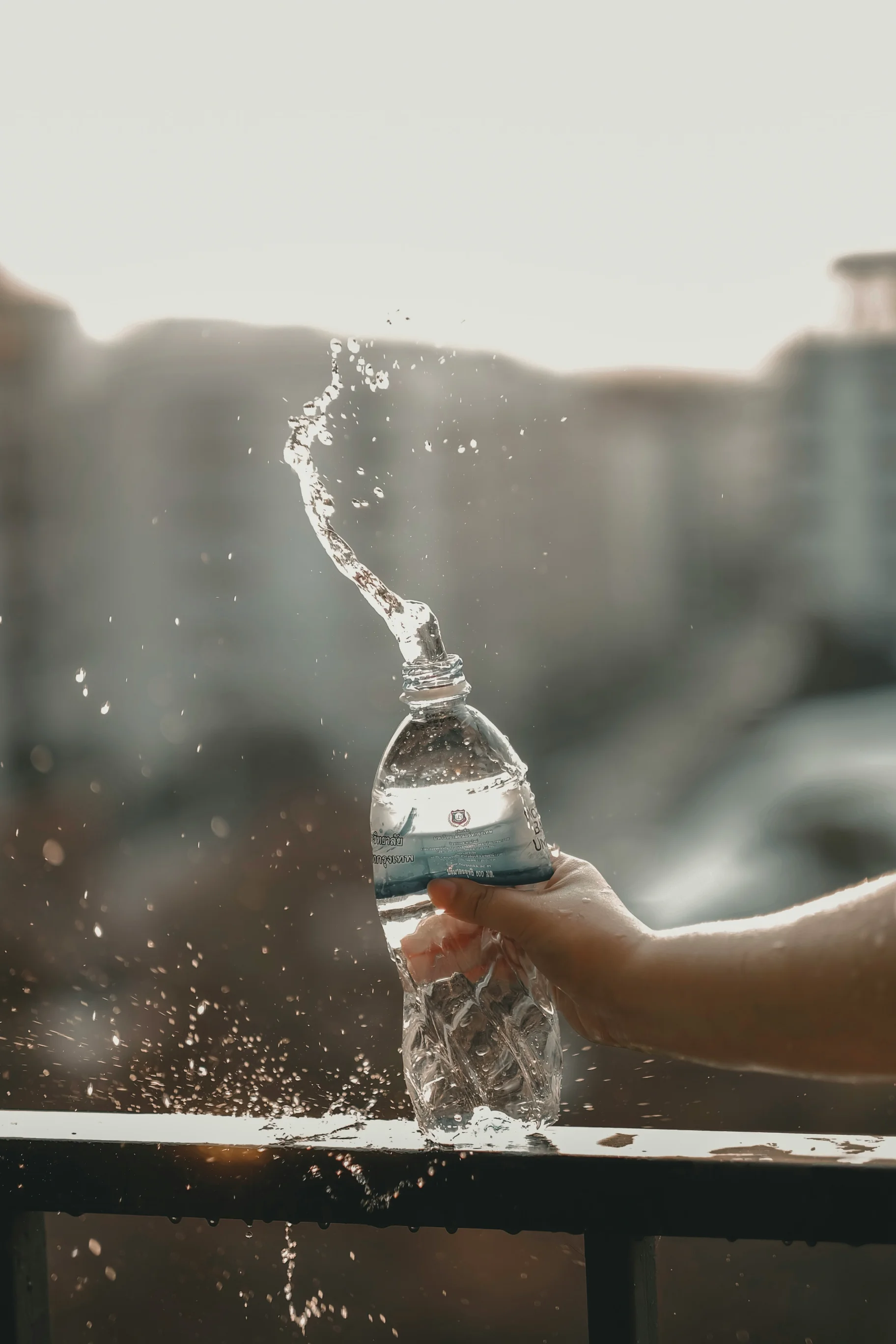 Hand squeezing a plastic water bottle, causing water to splash out.