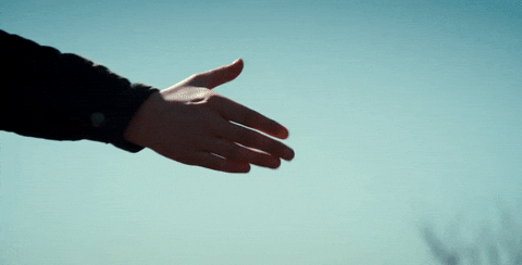 Hand reaches out against clear blue sky with blurred tree branches below.