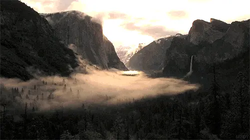 Valley with fog, surrounded by tall cliffs and mountains at sunset or sunrise light.