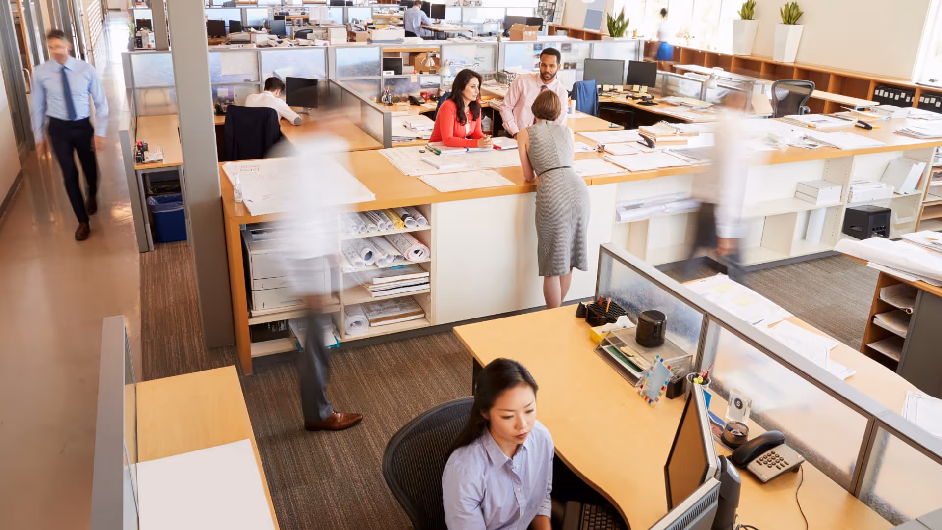 Office workers collaborating and working in a bright, open-plan office with desks and computers.