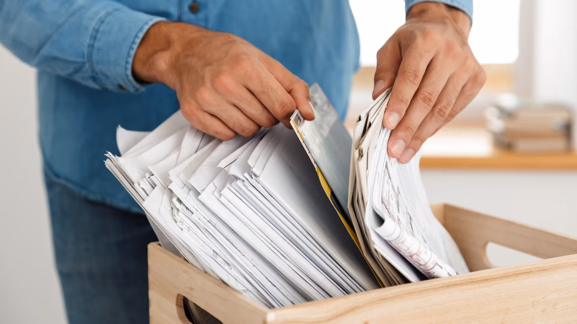Person organizing large stack of folded papers and blueprints in a wooden box.