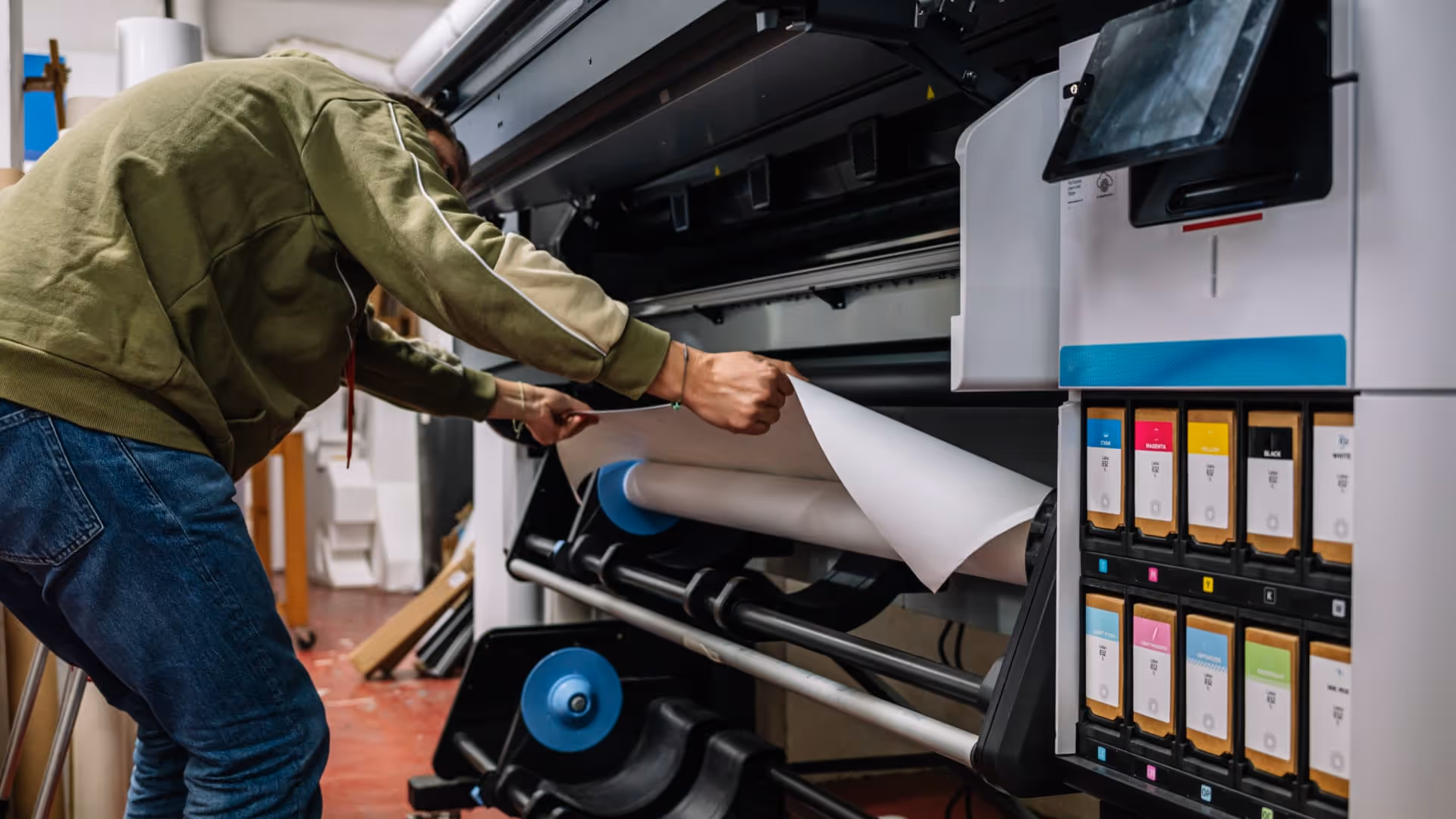 Man adjusting large roll of paper on an industrial printer with ink cartridges visible.