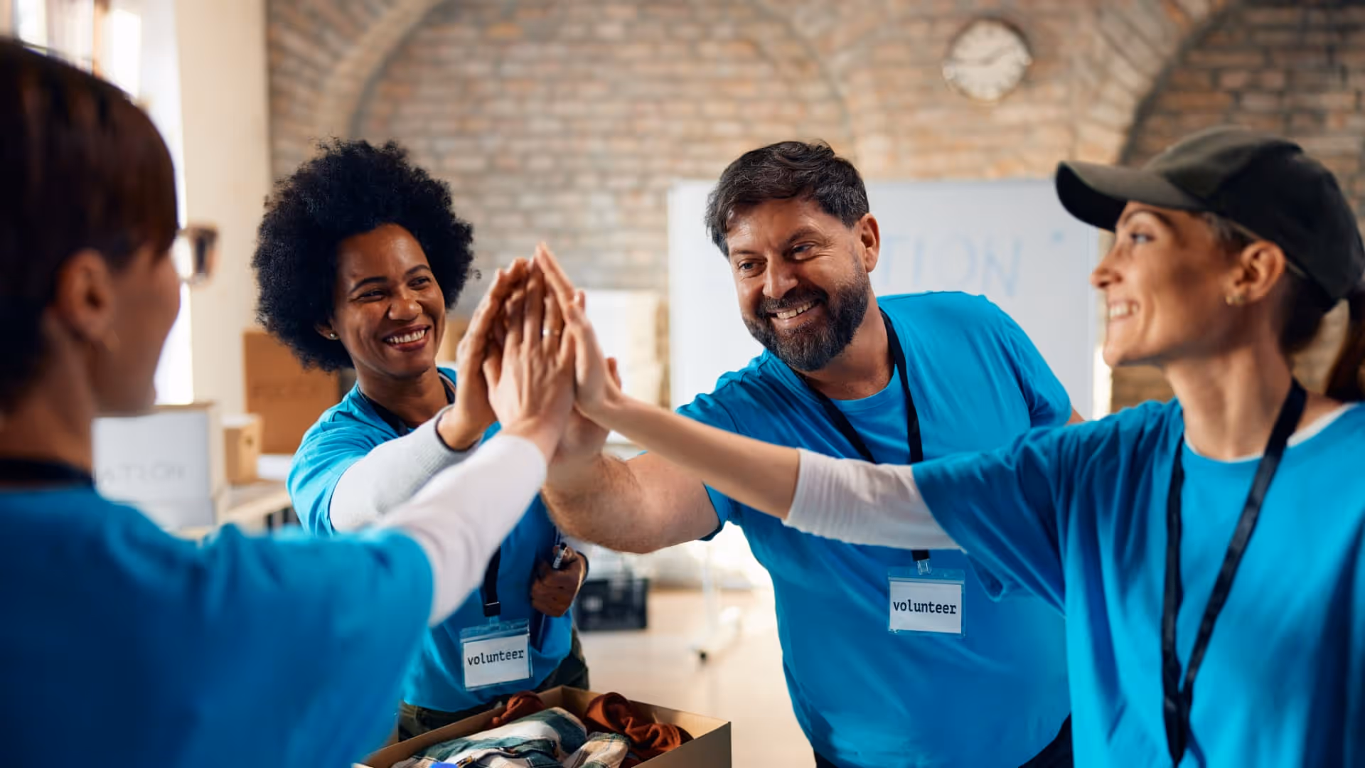 Smiling volunteers wearing blue shirts and badges giving a group high-five indoors.