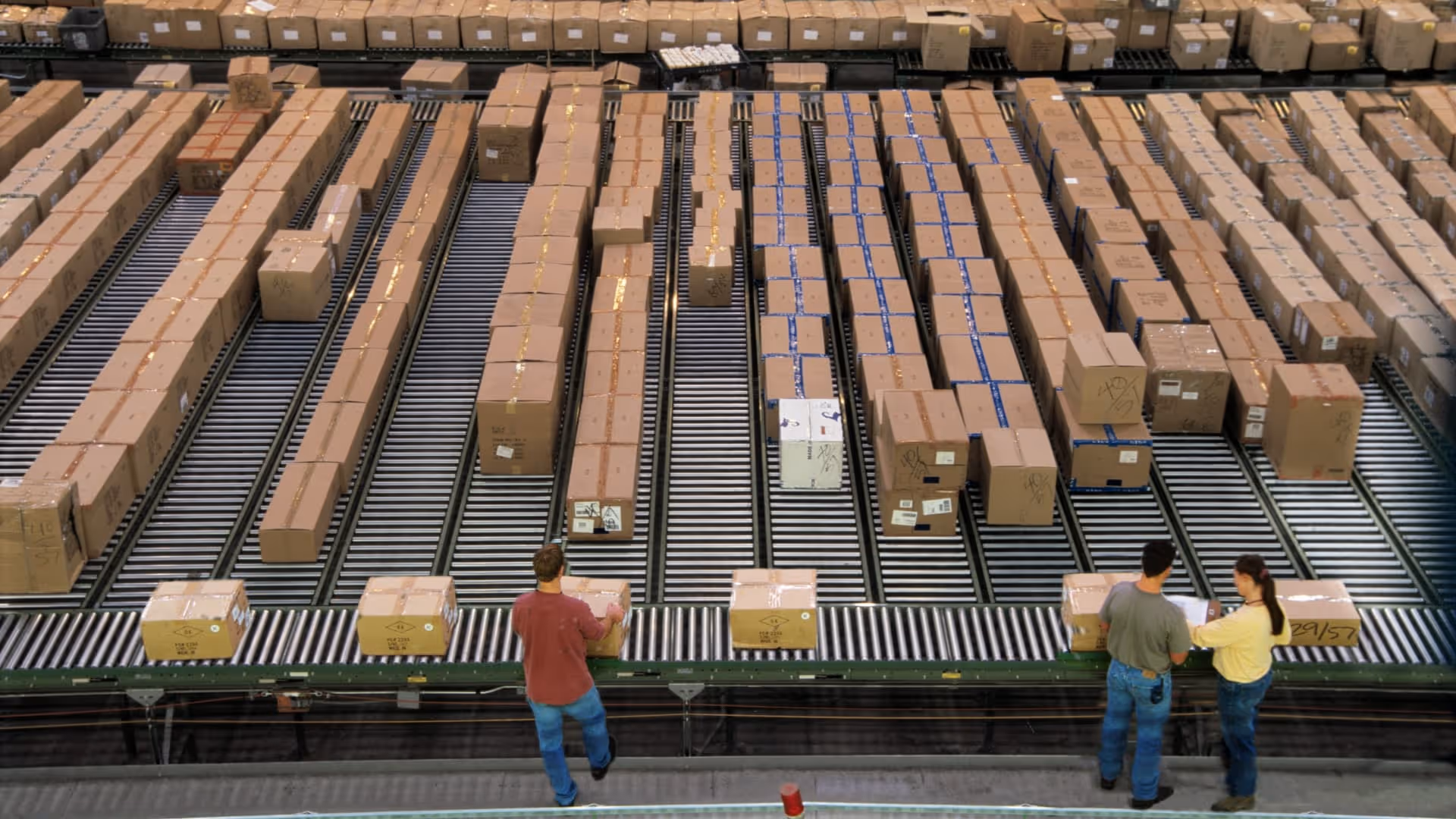 Workers sorting and organizing numerous cardboard boxes on conveyor belts in a large warehouse.