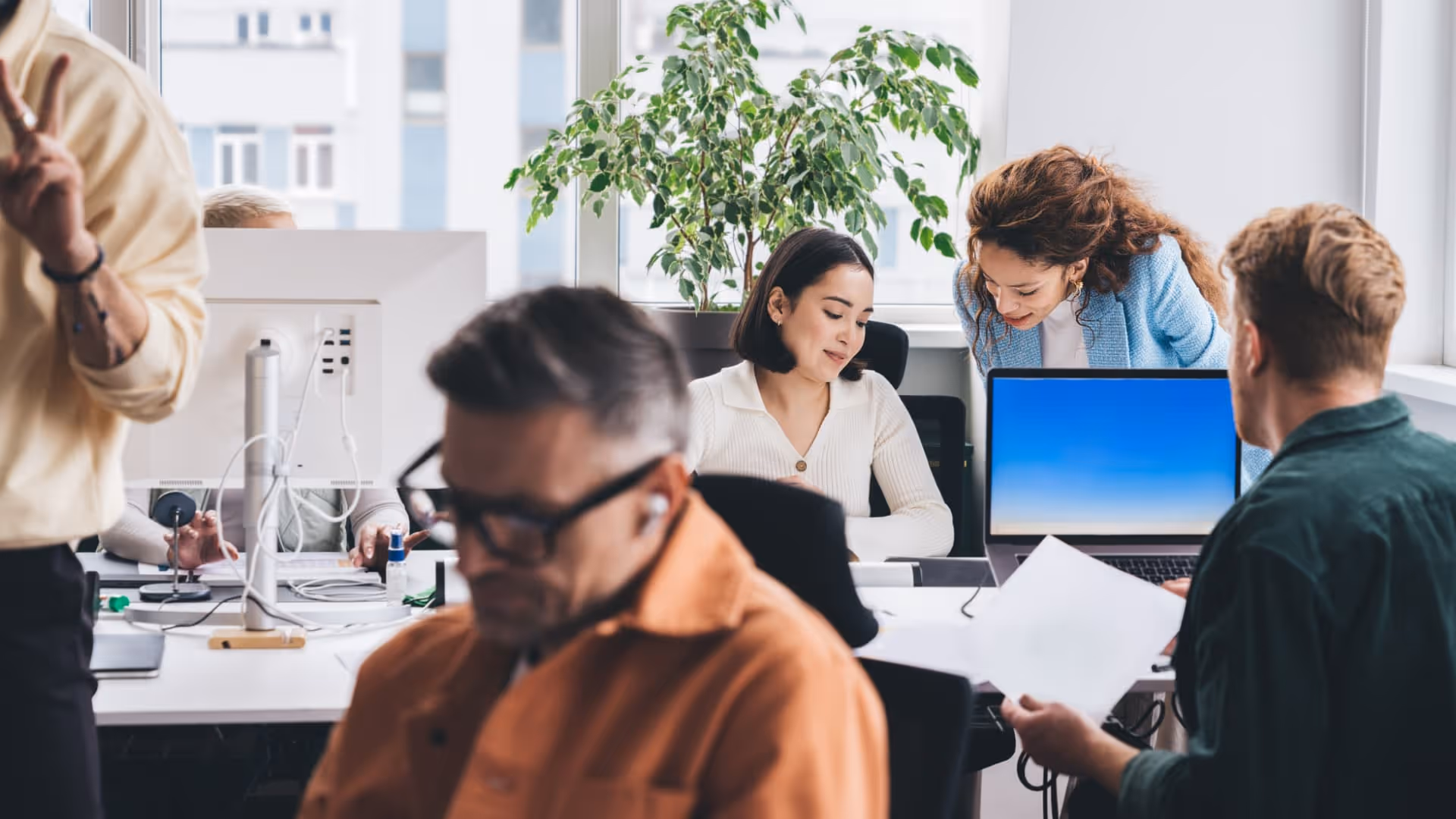 Diverse businesspeople collaborating and working at desks with computers in a bright office.