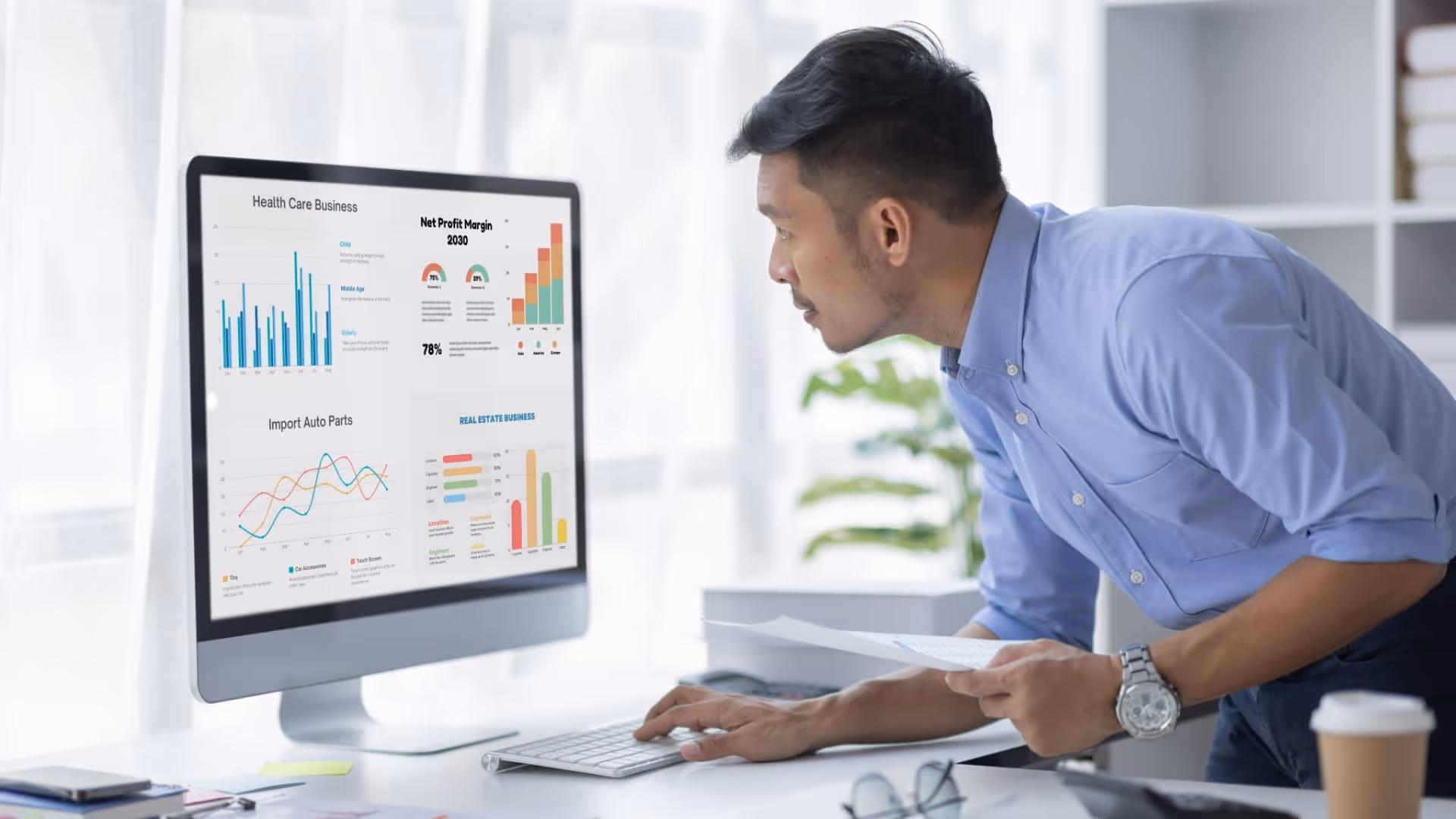 Man in blue shirt analyzing financial graphs on a computer screen in a bright office.