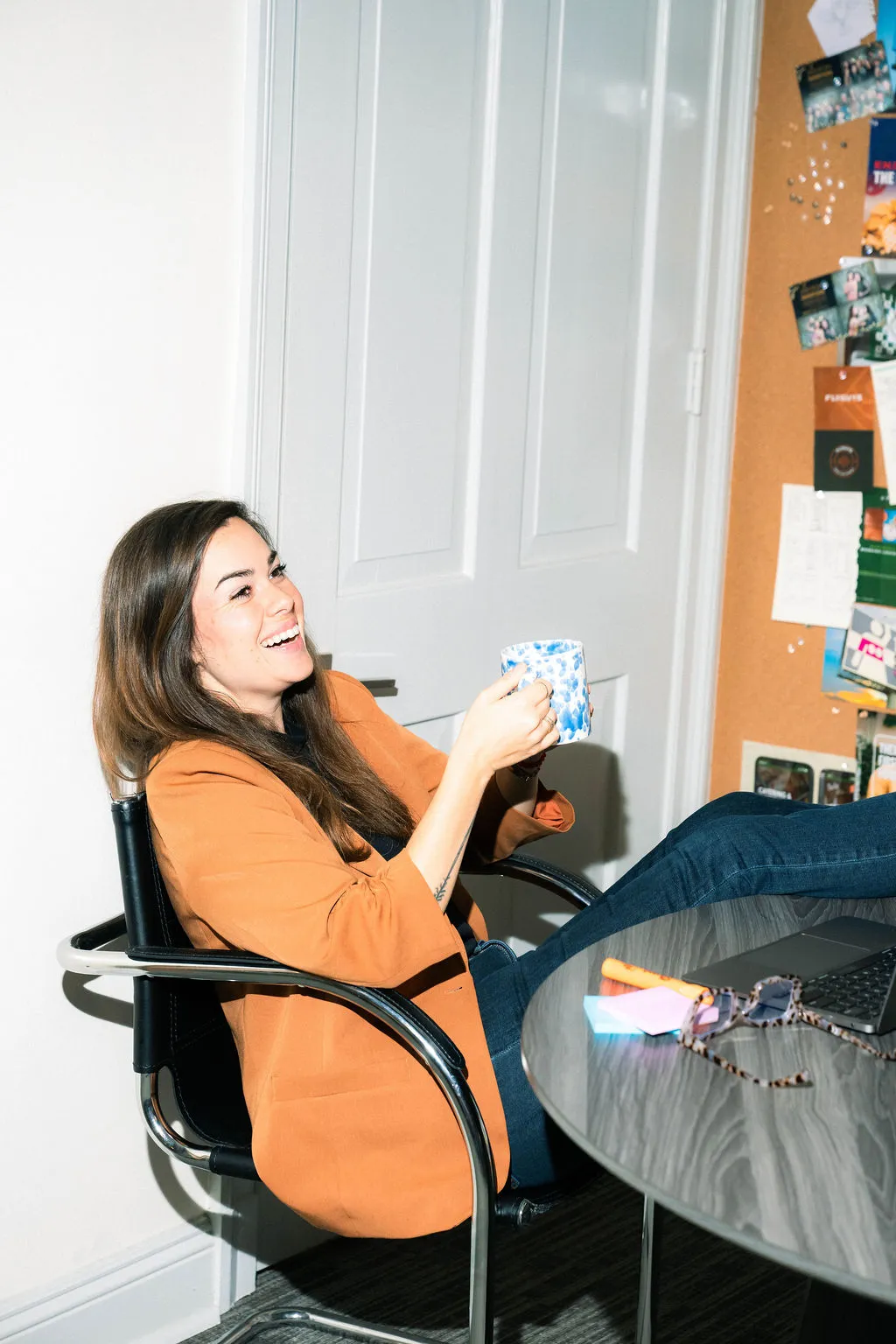 A woman in an orange blazer sitting at a desk holding a small package