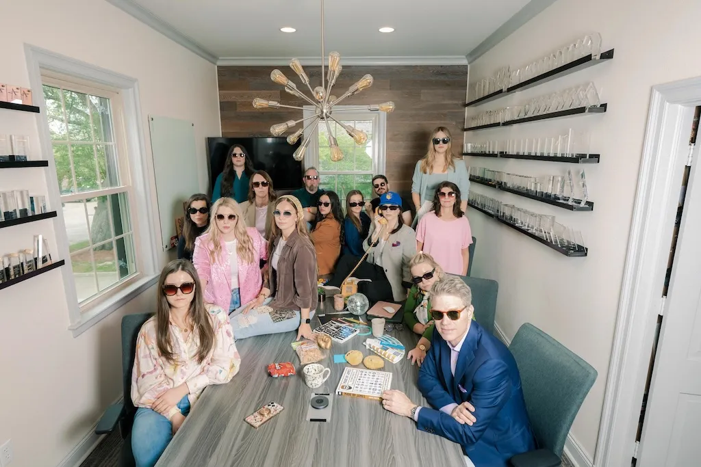The MESH team seated around a conference table wearing sunglasses during a bingo game