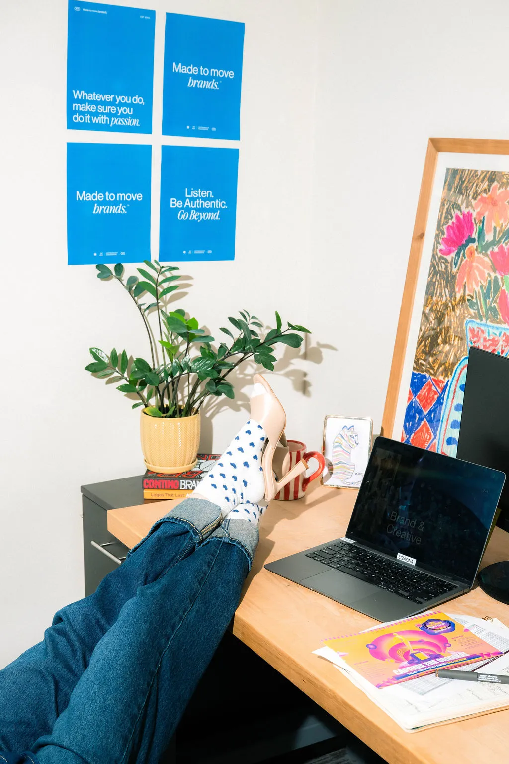 A person with their feet up on a desk beneath blue MESH posters reading Made to Move Brands and Listen. Be Authentic. Go Beyond.