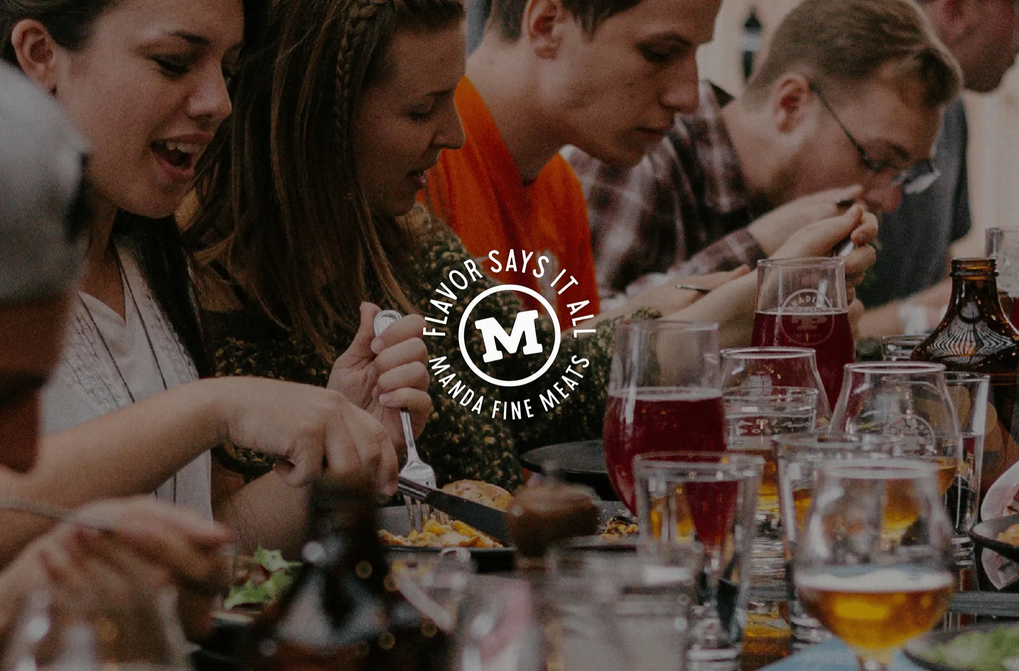People sharing a meal at a long table, with the Manda Flavor Says It All badge overlaid