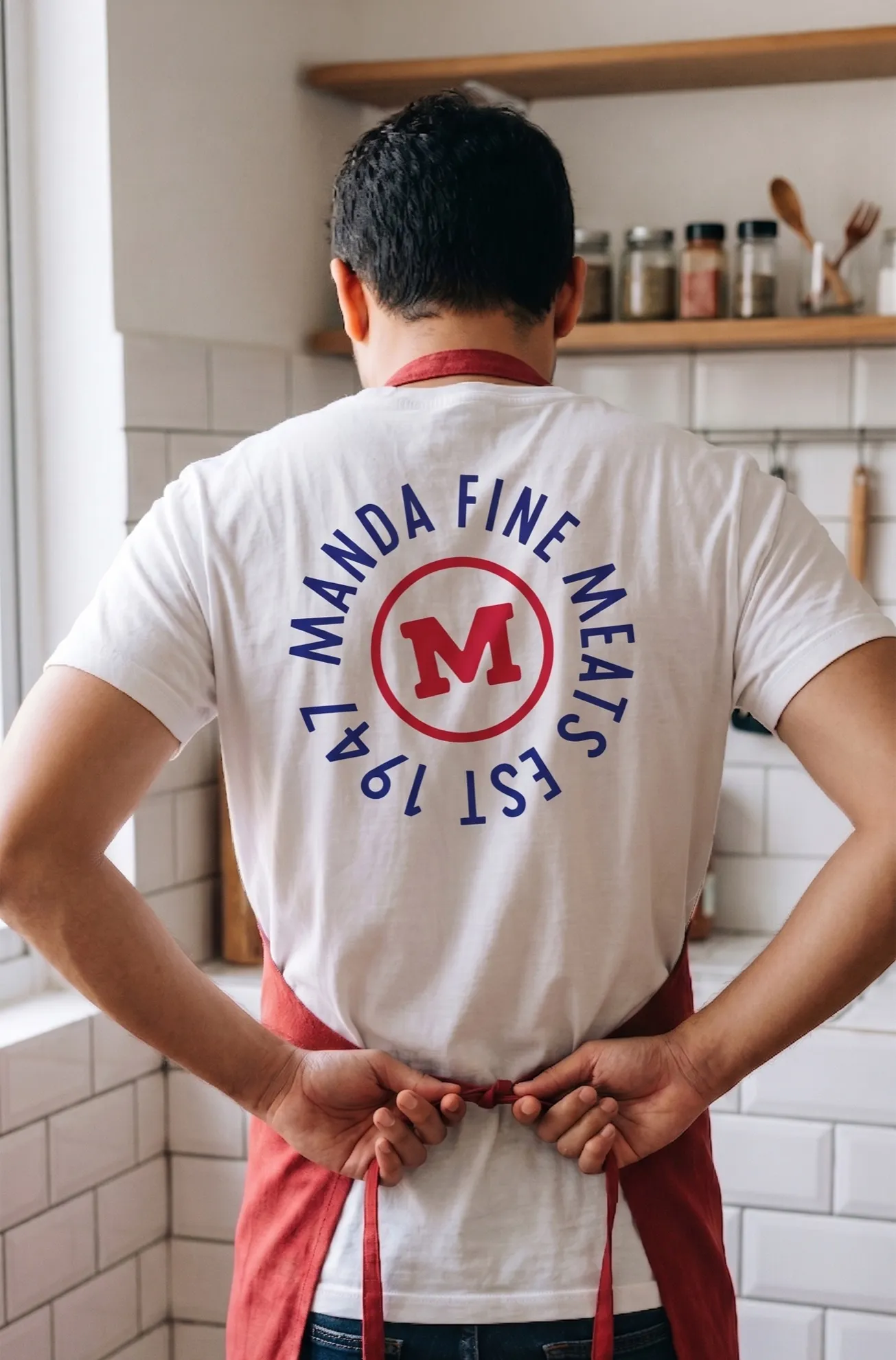 A person seen from behind wearing a Manda Fine Meats t-shirt in a kitchen