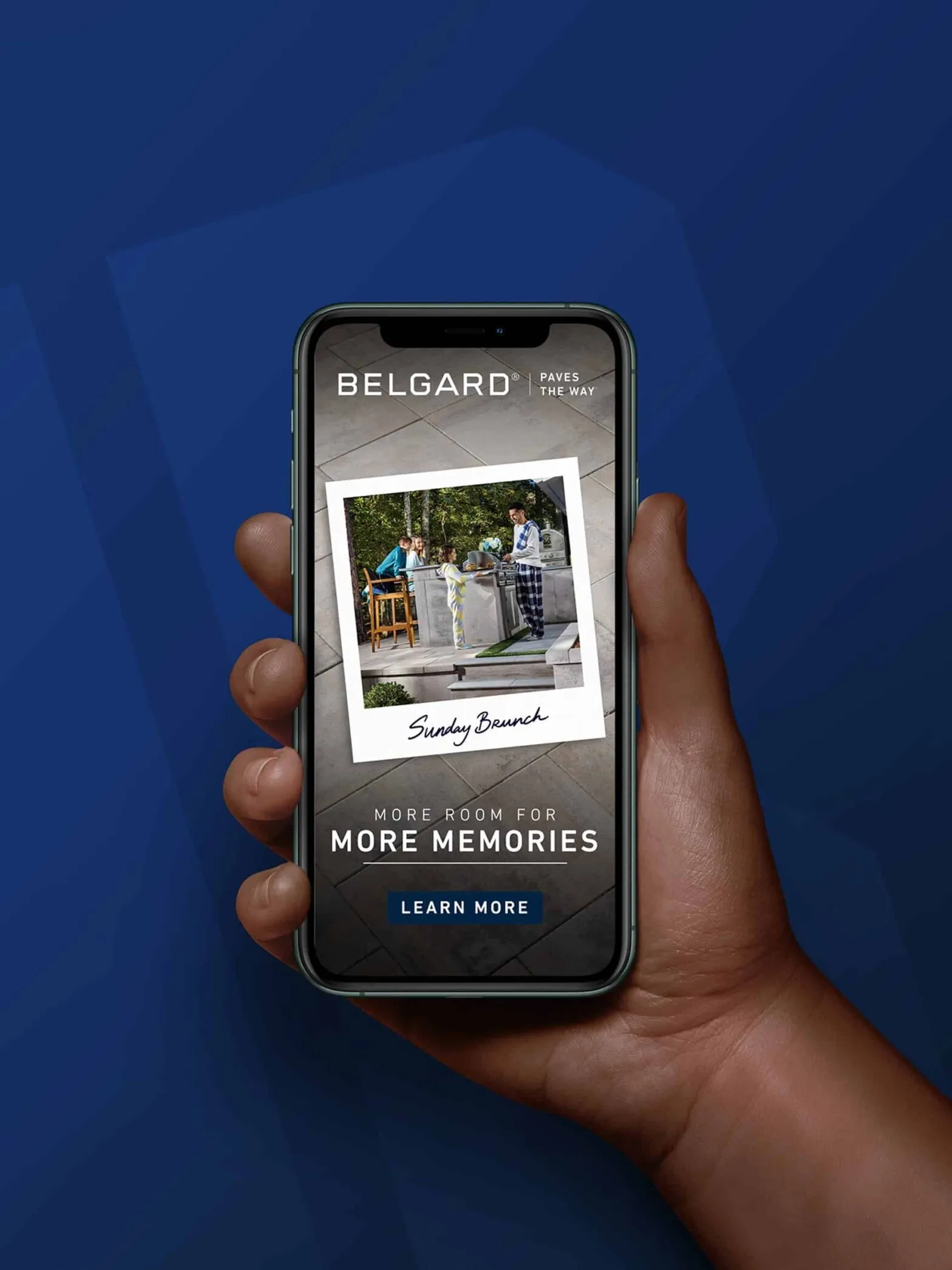 A hand holding a phone showing a Belgard ad reading Fill It With More Memories