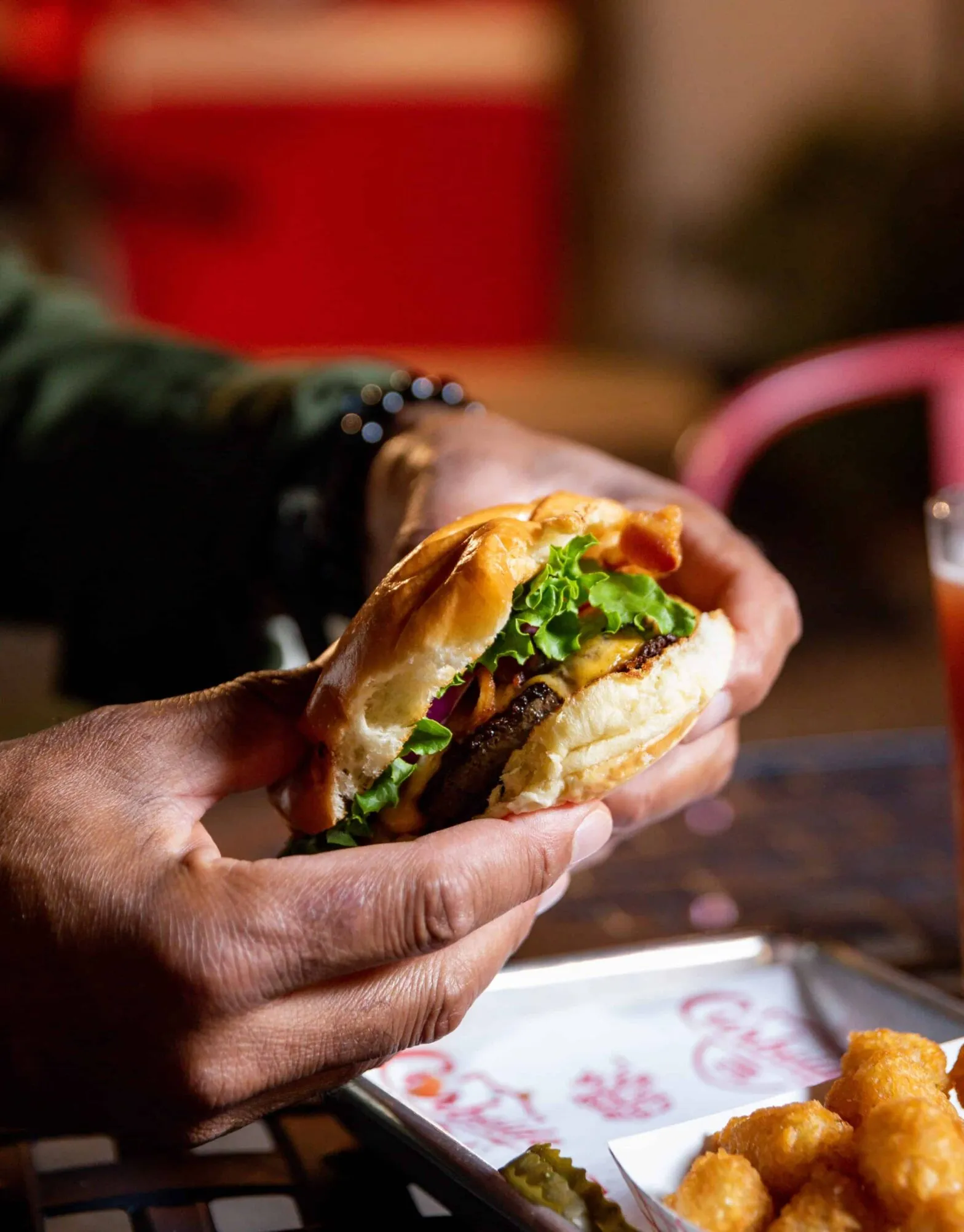 Hands holding a burger over a basket of fried food
