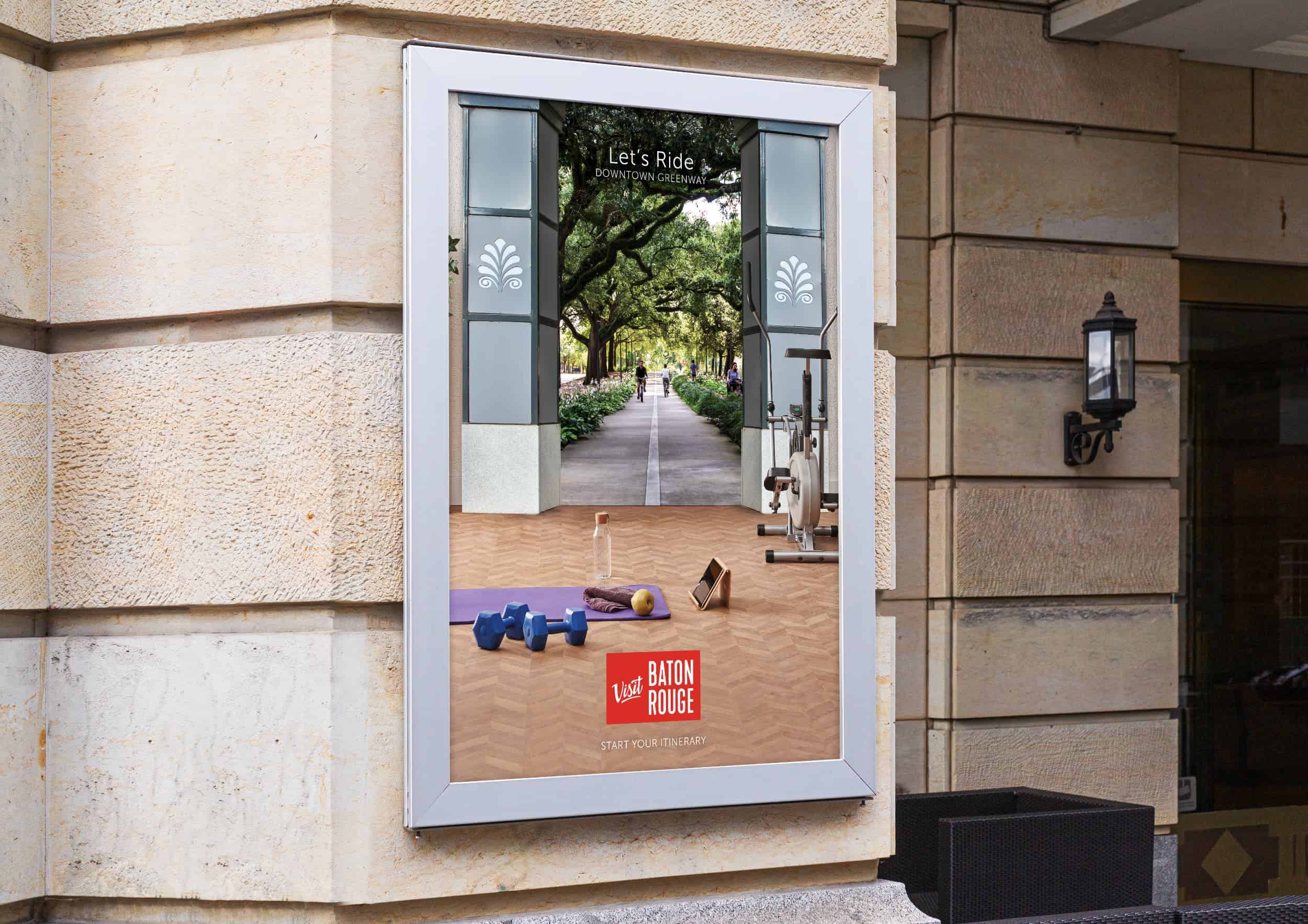 A Visit Baton Rouge poster showing an oak-lined road, mounted on a stone building
