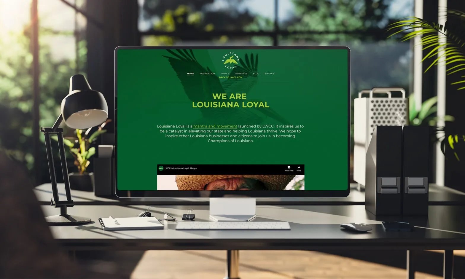 A desktop screen on a studio desk showing the LWCC site headlined We Are Louisiana Loyal