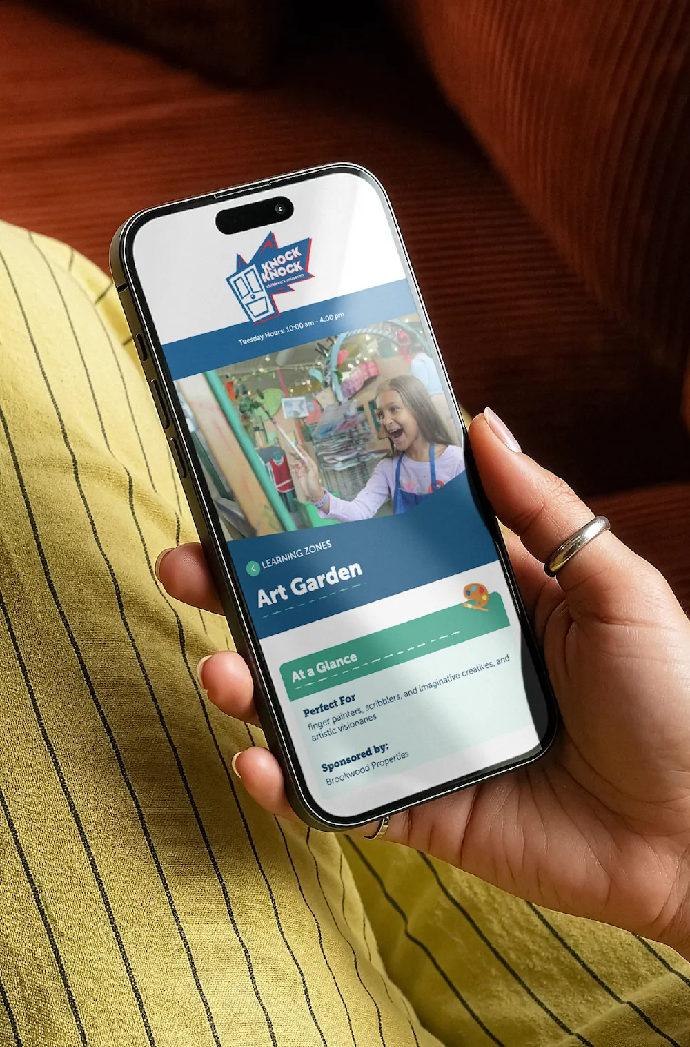 A hand holding a phone showing the Knock Knock Children's Museum exhibits page