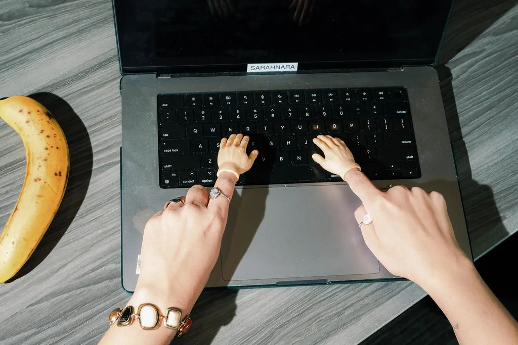 A laptop with small fingers typing with a banana on a table