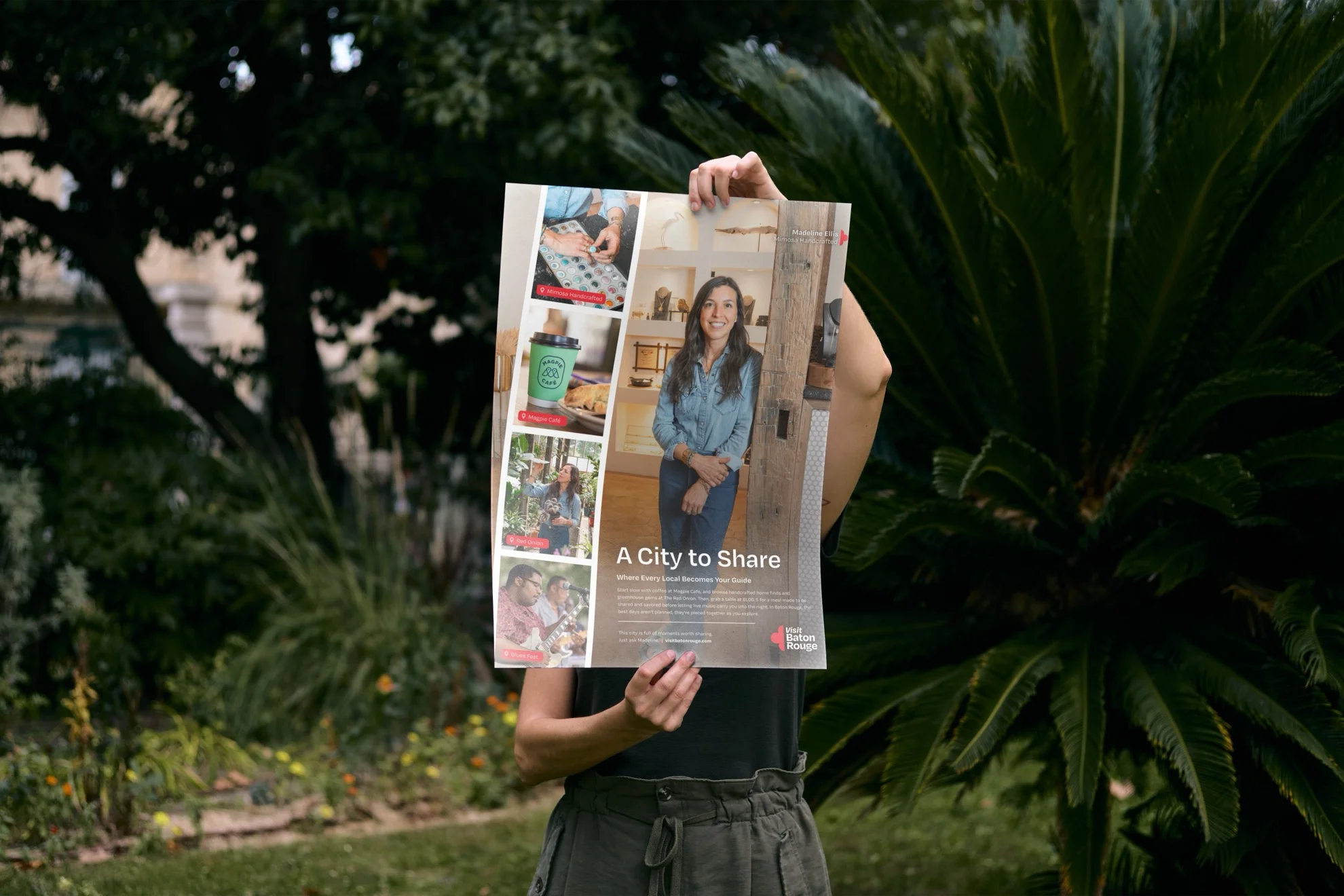 A person holding up a Visit Baton Rouge A City to Share poster outdoors