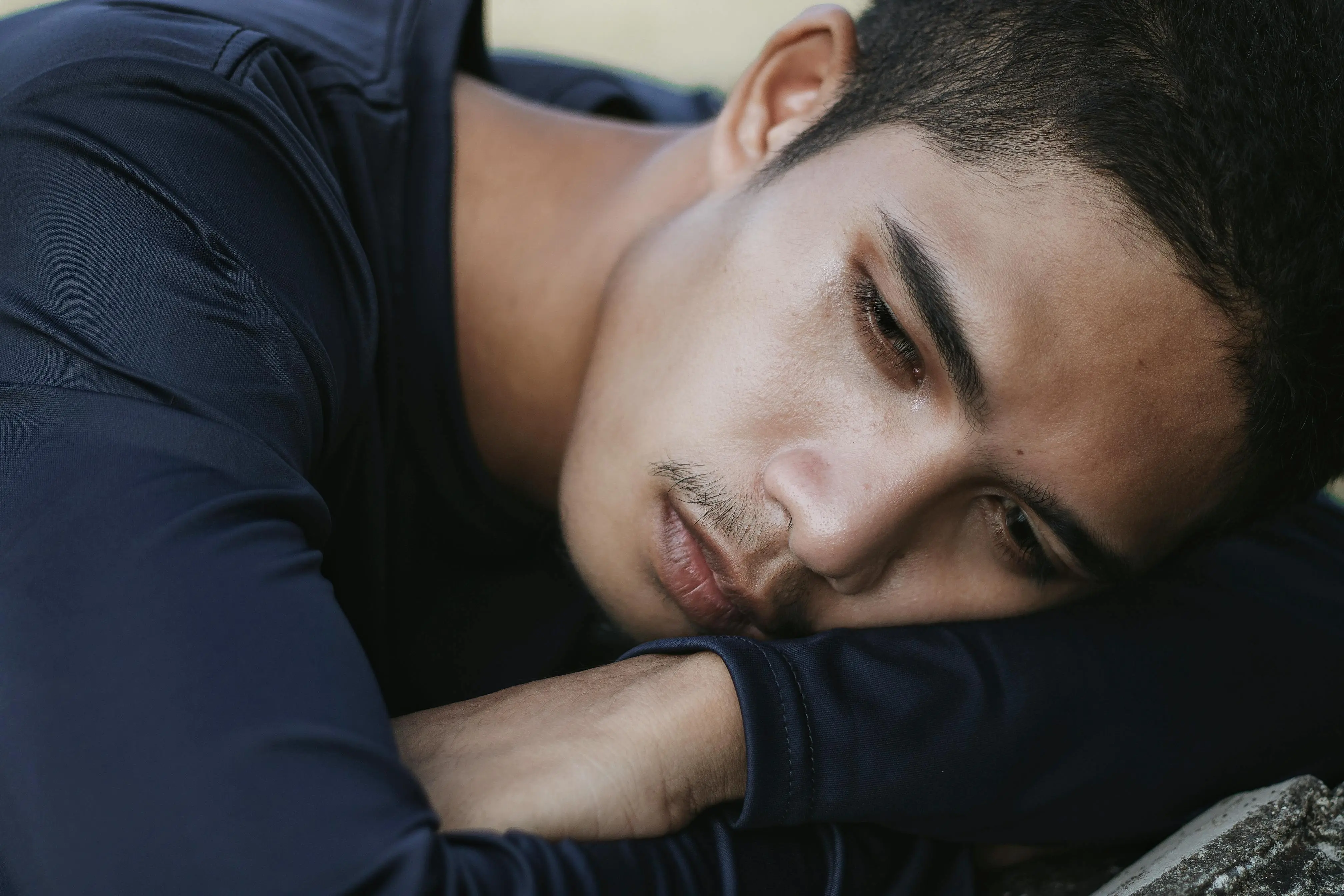 Close-up of a young man resting his head on his folded arms, appearing contemplative or sad.