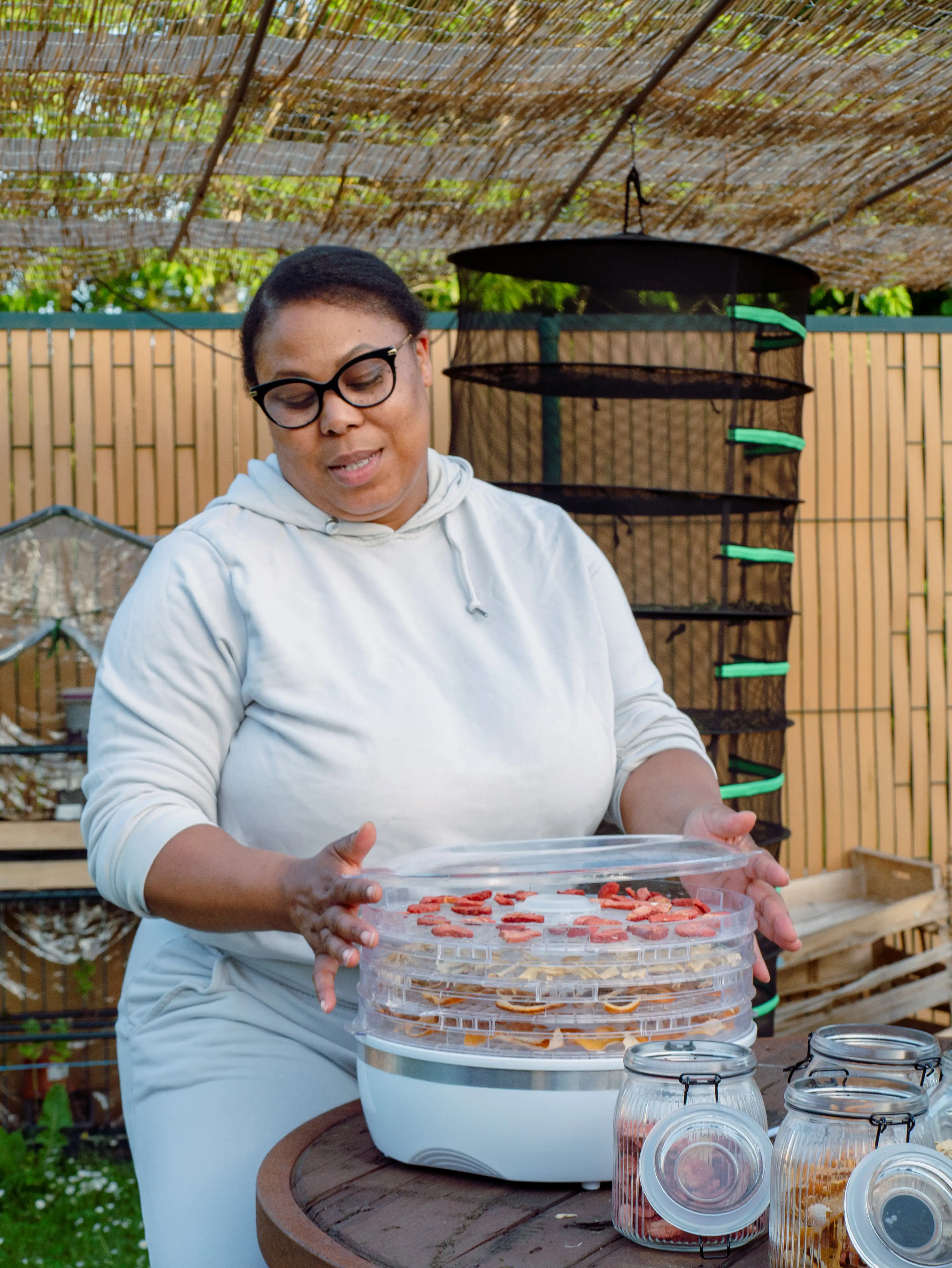 Femme manipulant un déshydrateur alimentaire avec tranches de fruits sur une table en bois.