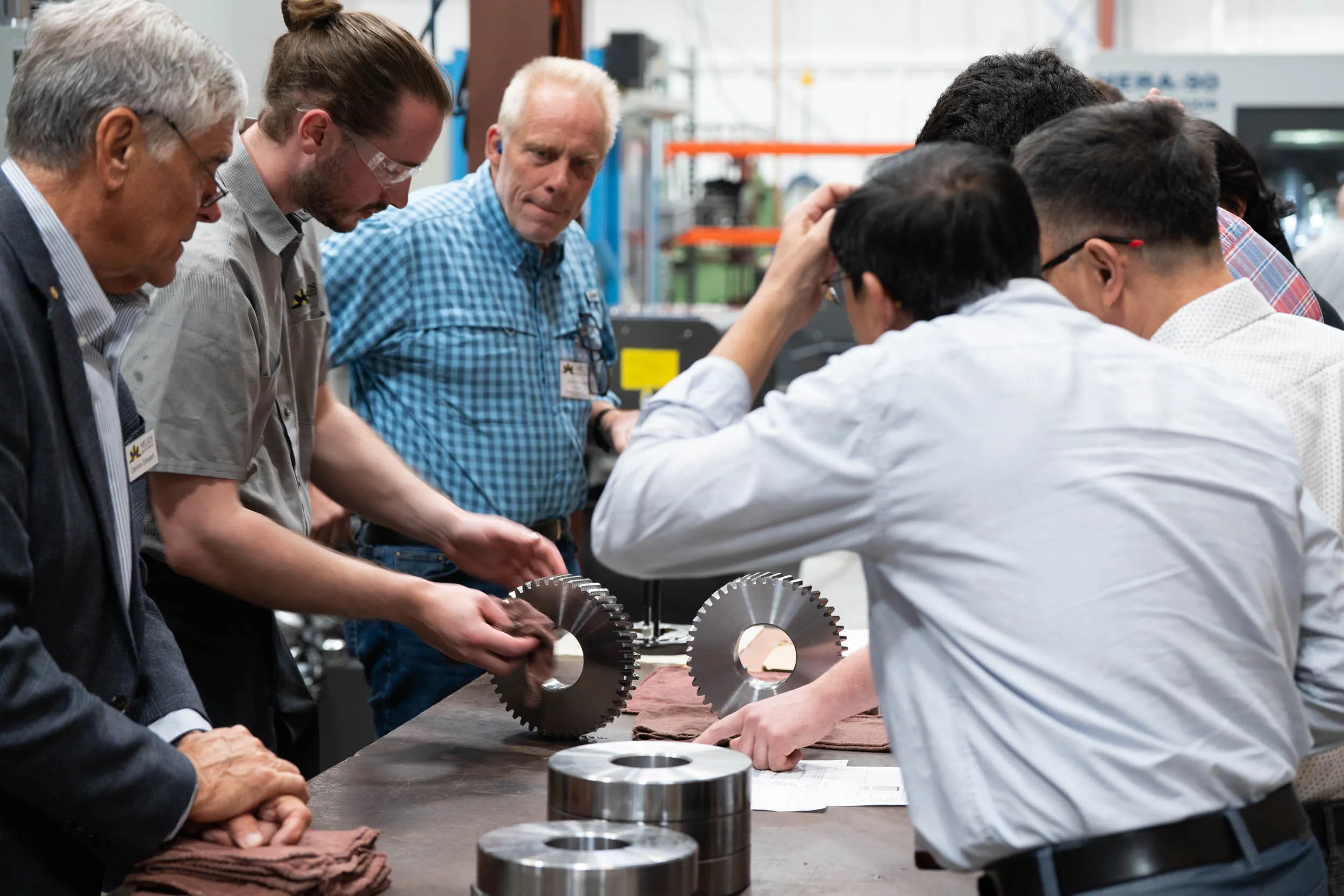 Helios Gear School attendees examining a gear and cutting tools around a shop-floor table