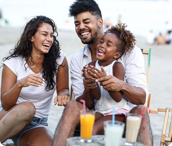 Smiling family of three sitting on beach chairs with drinks on a table, enjoying time together.