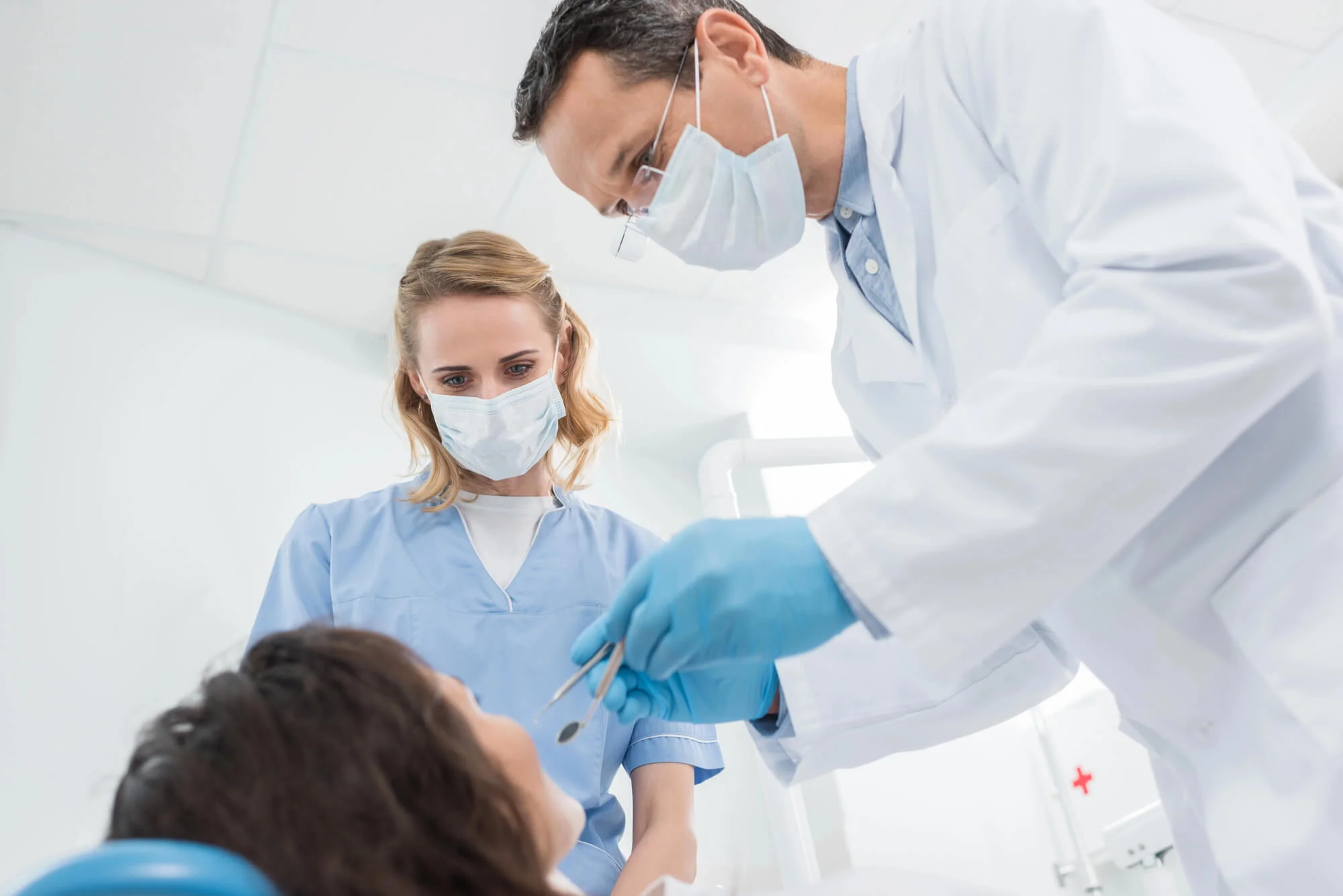 Dentist and dental assistant wearing masks examining a patient in a dental clinic.