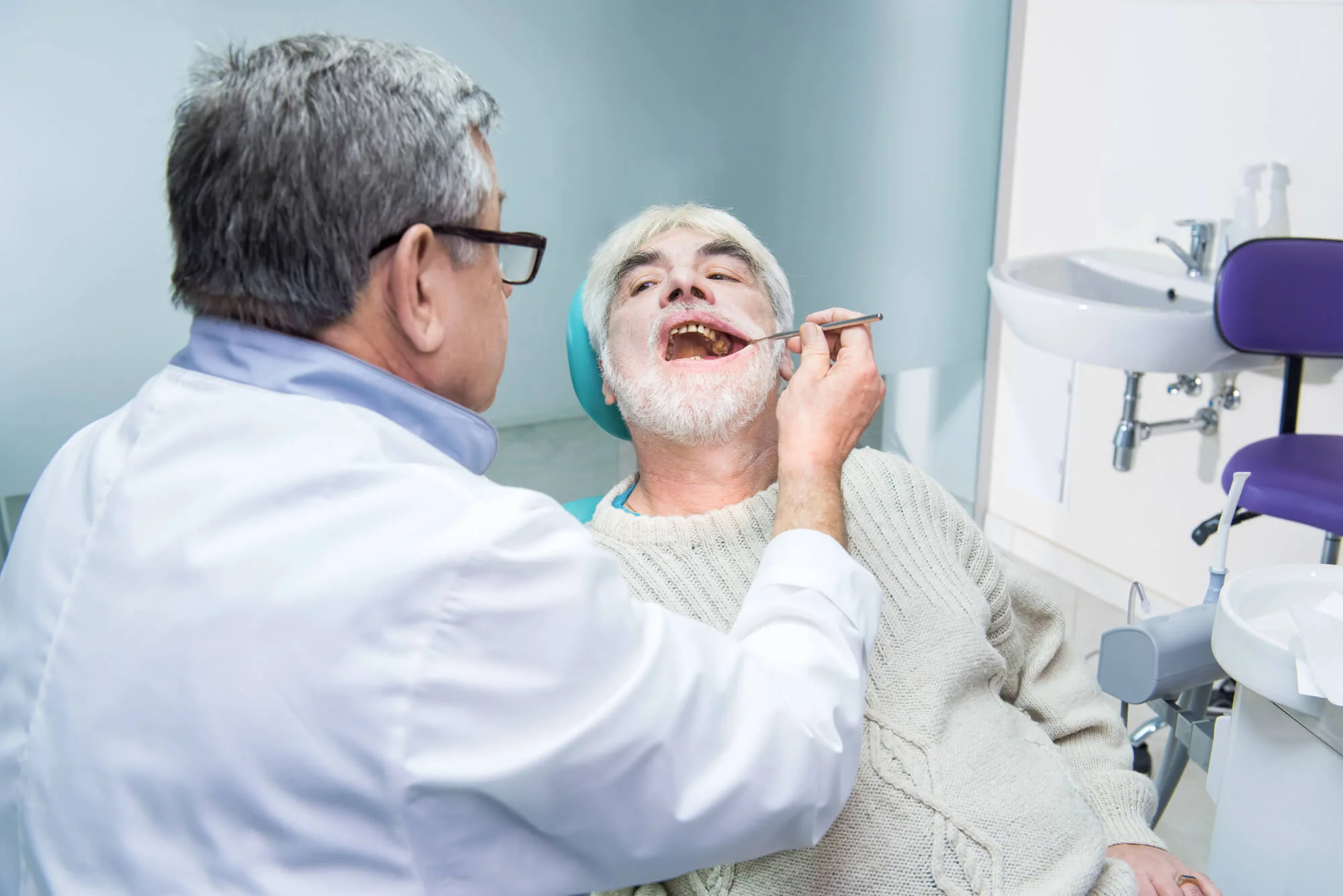 Elderly man with white beard having his teeth examined by a dentist in a dental clinic.