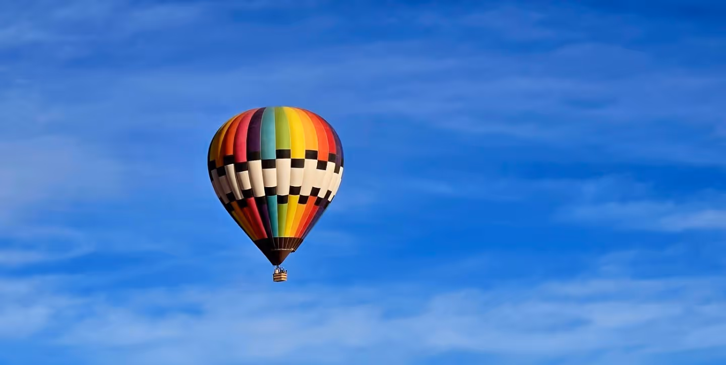 Colorful hot air balloon with vertical stripes and a checkered middle band flying in a clear blue sky.