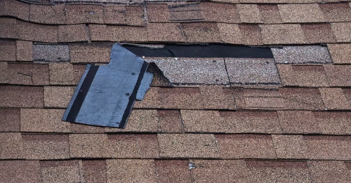 Damaged roof shingles peeling and missing exposing underlayment after storm damage