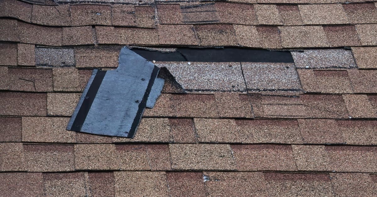 Damaged roof shingles peeling and missing exposing underlayment after storm damage