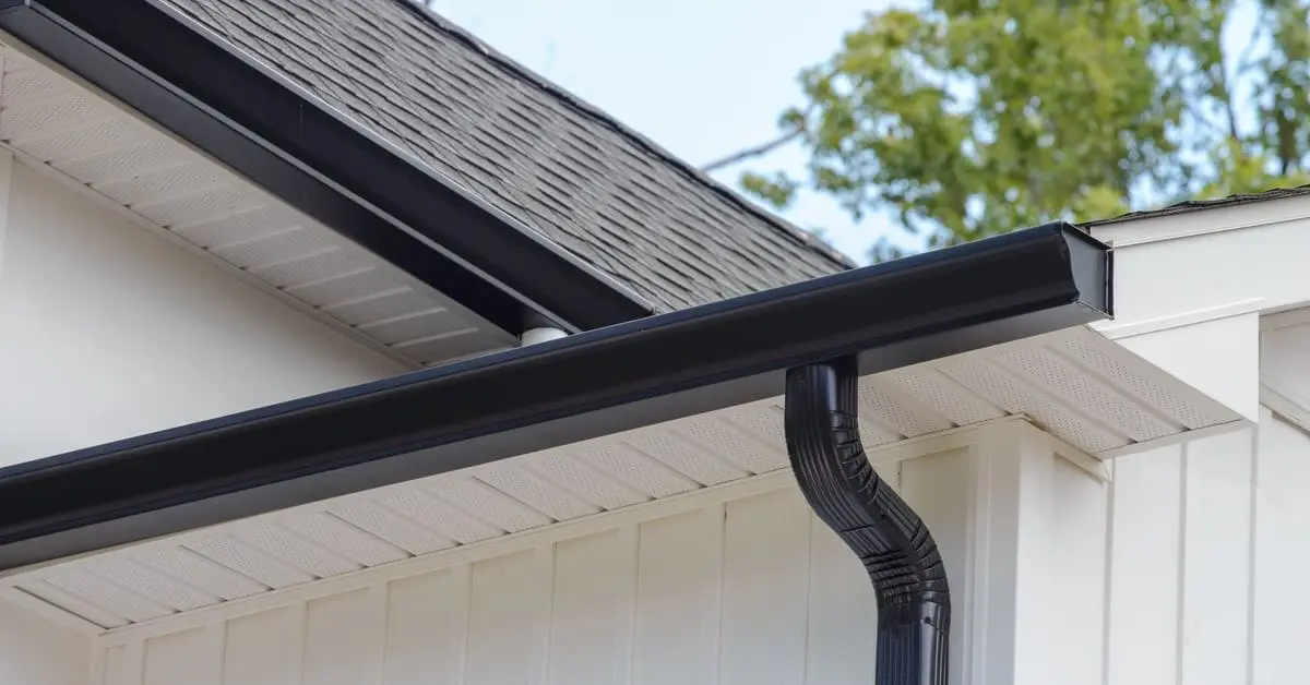 Black gutter and downspout system installed along roof edge directing water away from home
