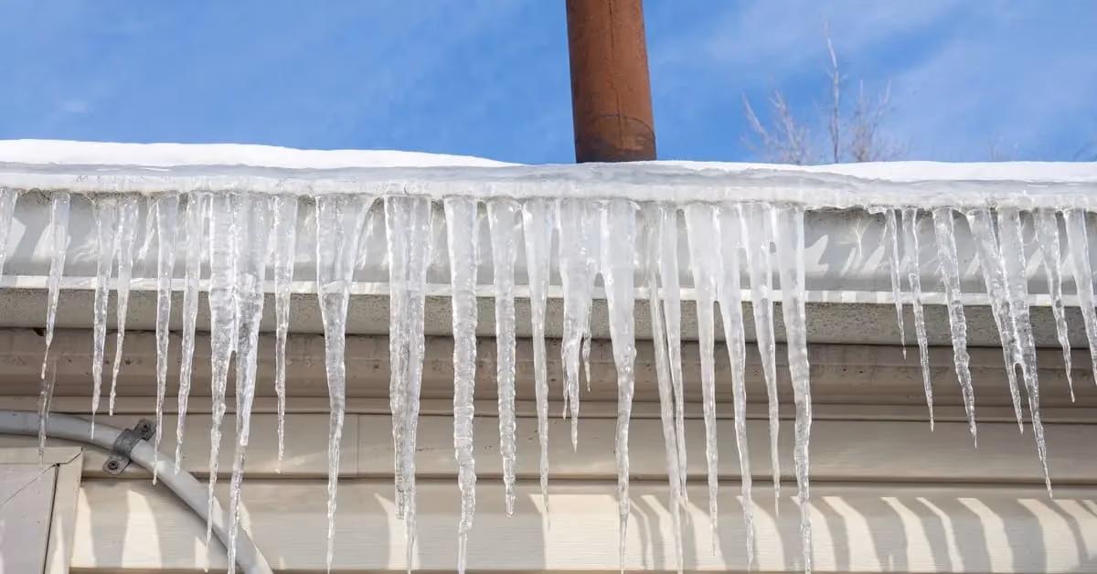 Icicles hanging from roof edge and gutter showing early signs of ice dam formation in winter