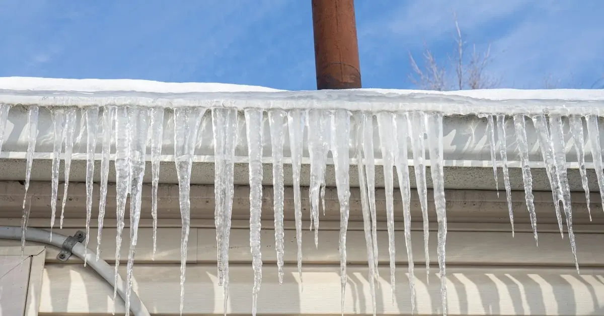 Icicles hanging from roof edge and gutter showing early signs of ice dam formation in winter