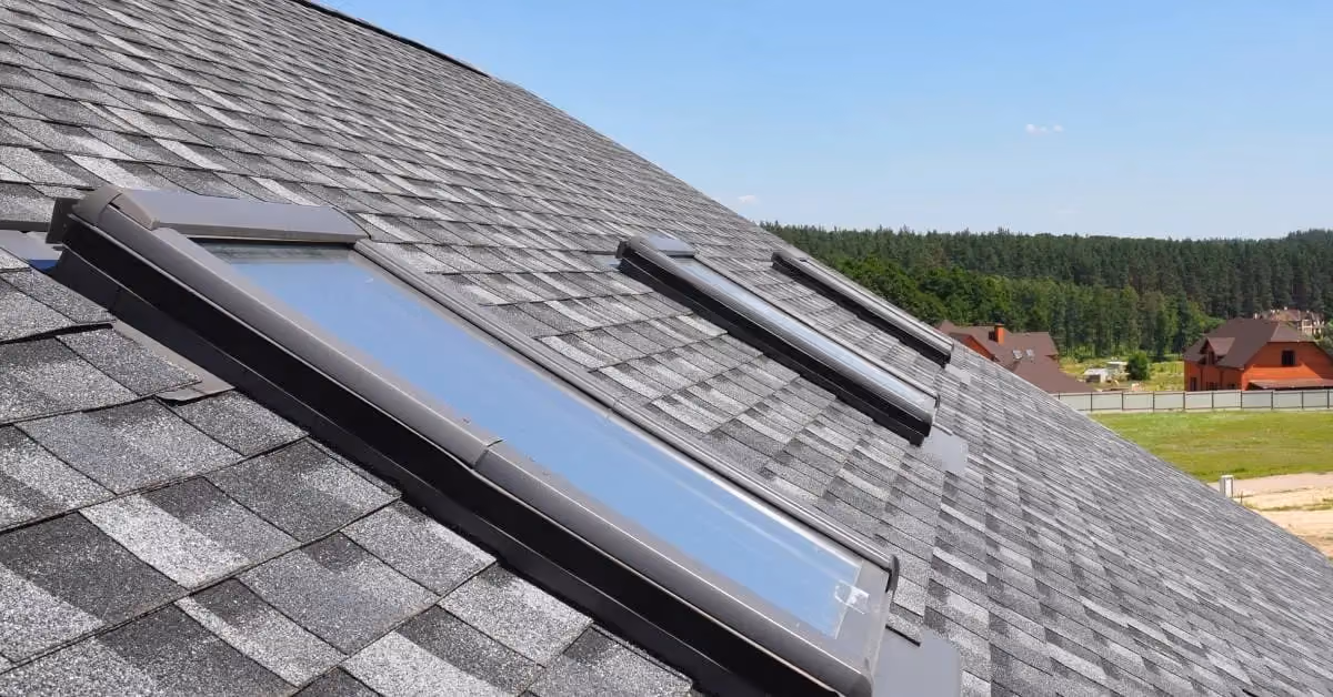 Roof with three rectangular skylights installed on dark asphalt shingles overlooking residential neighborhood
