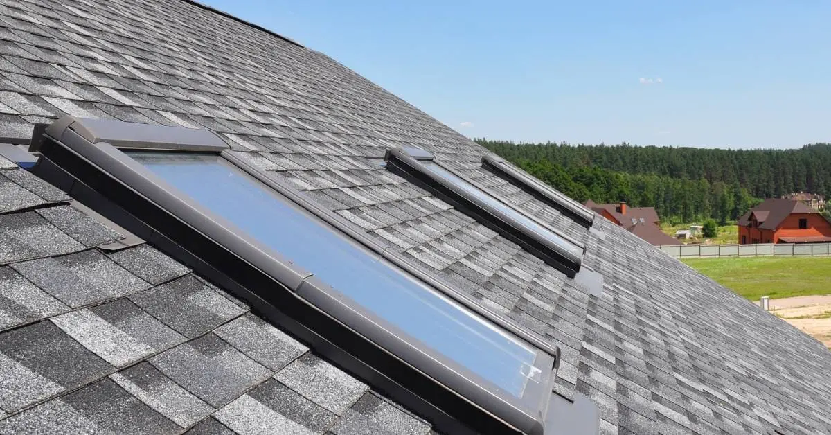Roof with three rectangular skylights installed on dark asphalt shingles overlooking residential neighborhood
