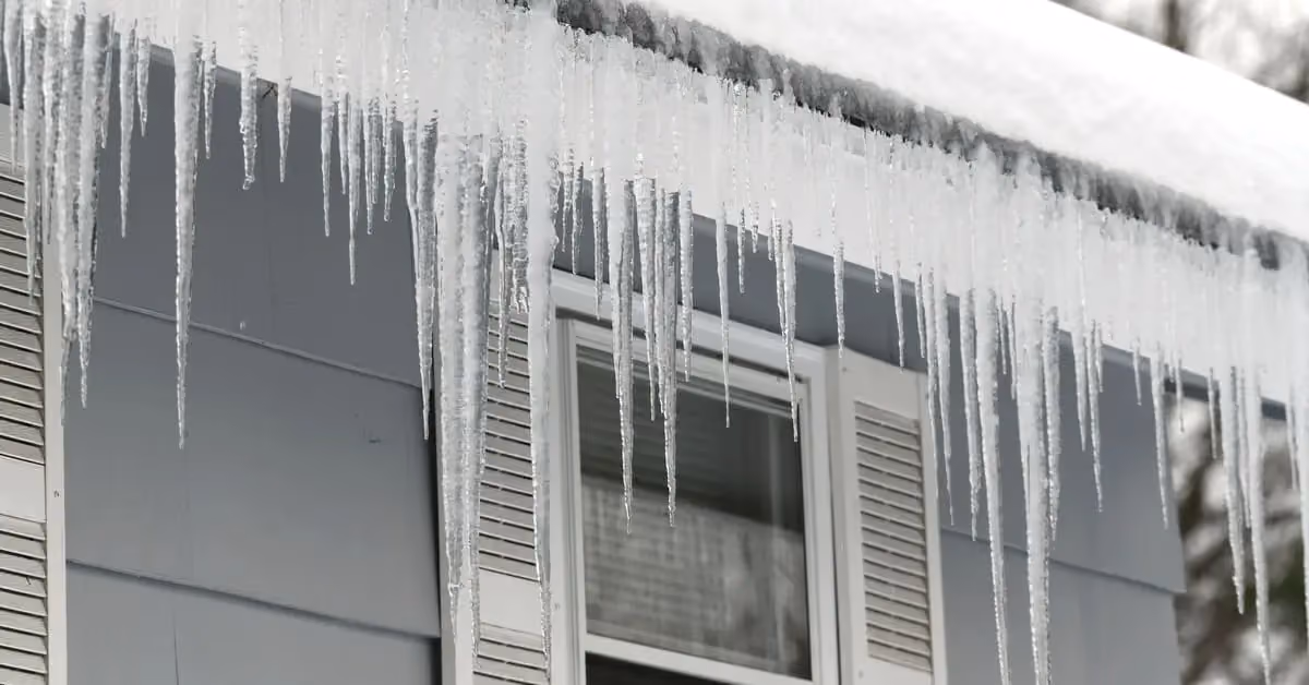 Long icicles hanging from roof edge and gutter on home showing ice dam buildup in winter