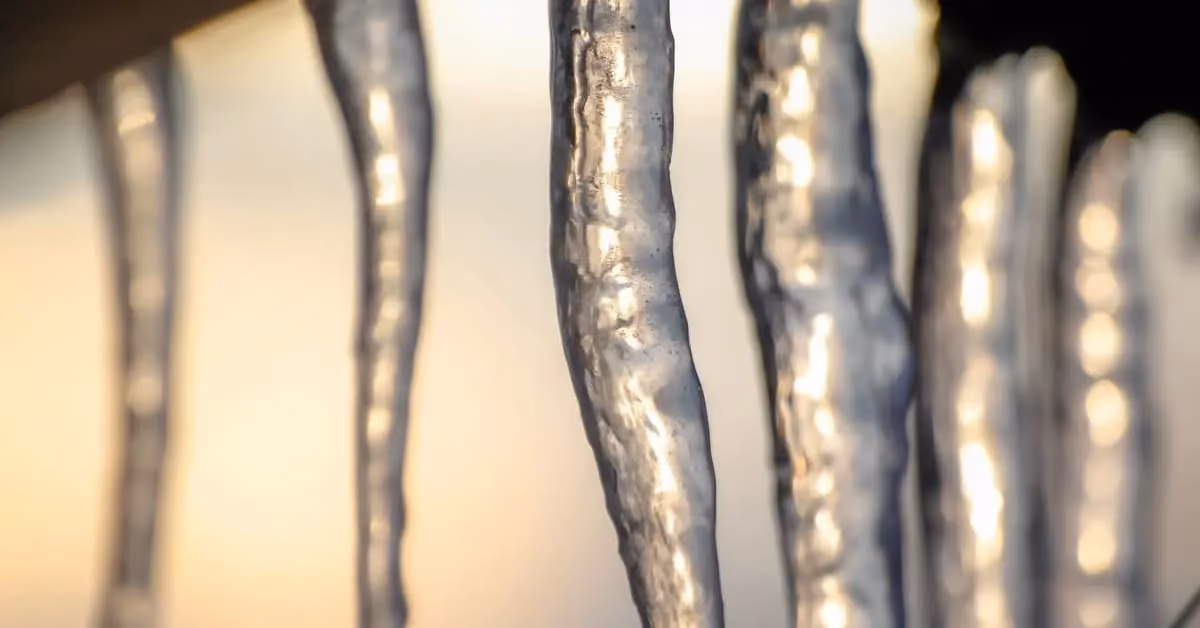 Close-up of icicles hanging from roof edge showing early ice dam formation in winter sunlight