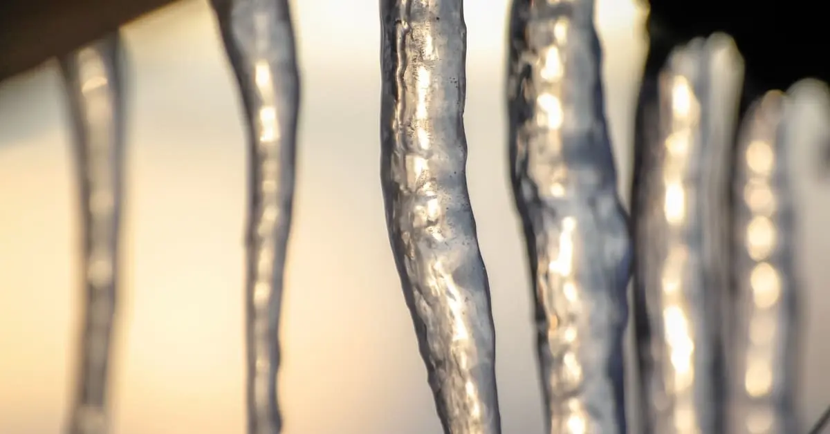 Close-up of icicles hanging from roof edge showing early ice dam formation in winter sunlight