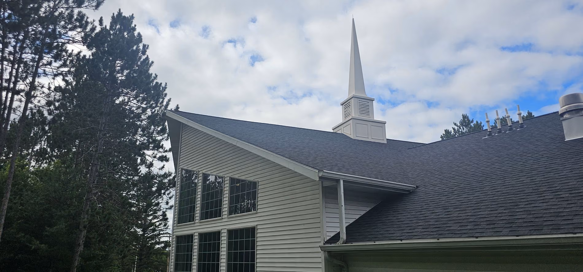 Completed church roof replacement in Merrill, WI showing the finished dark shingle roof and white steeple.