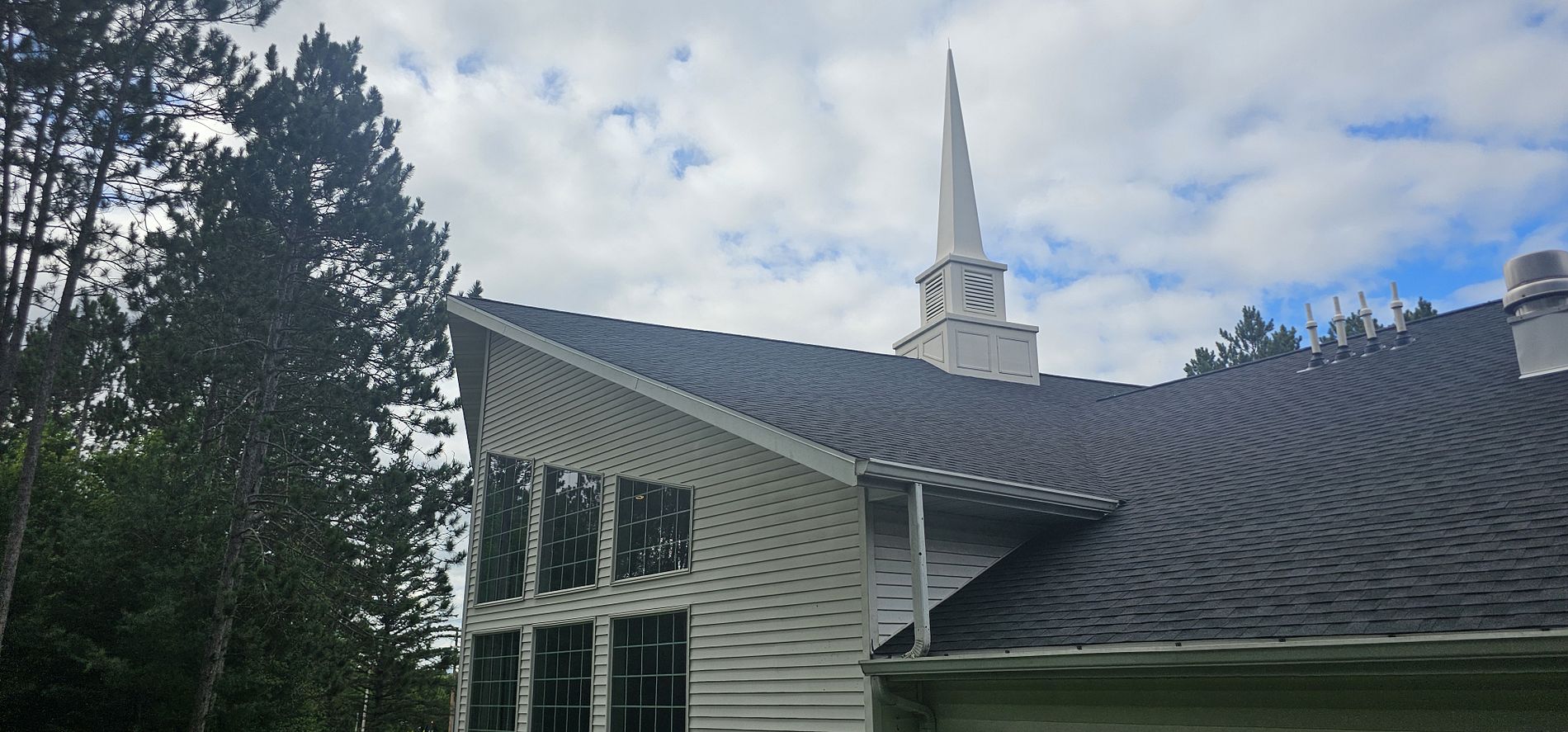 Completed church roof replacement in Merrill, WI showing the finished dark shingle roof and white steeple.