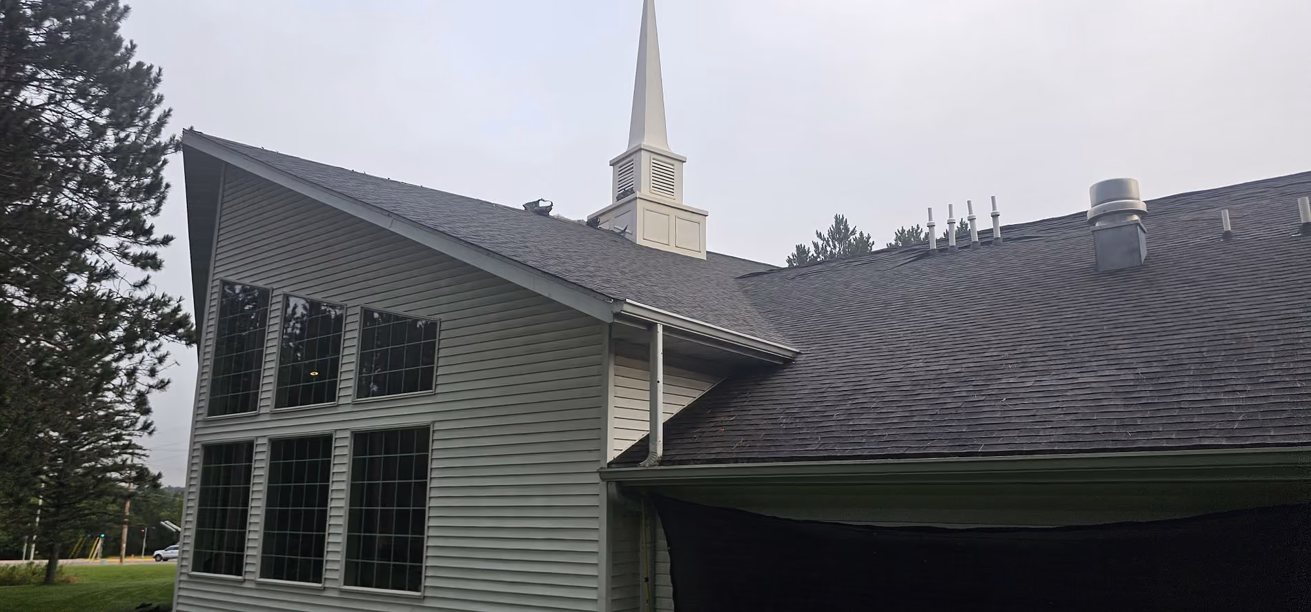 Large church roof replacement in Merrill, WI with new dark shingles installed around the steeple and roof vents.