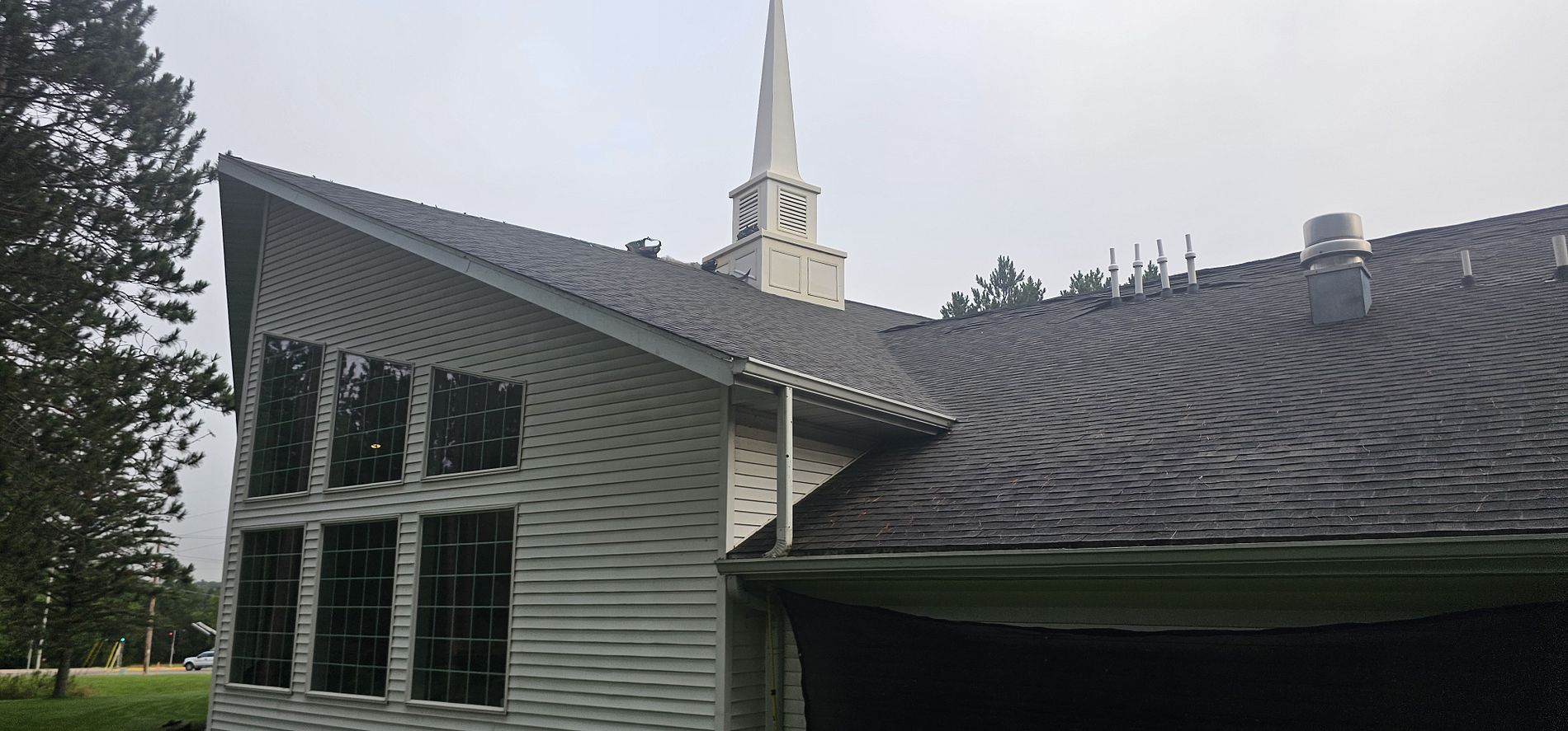 Large church roof replacement in Merrill, WI with new dark shingles installed around the steeple and roof vents.