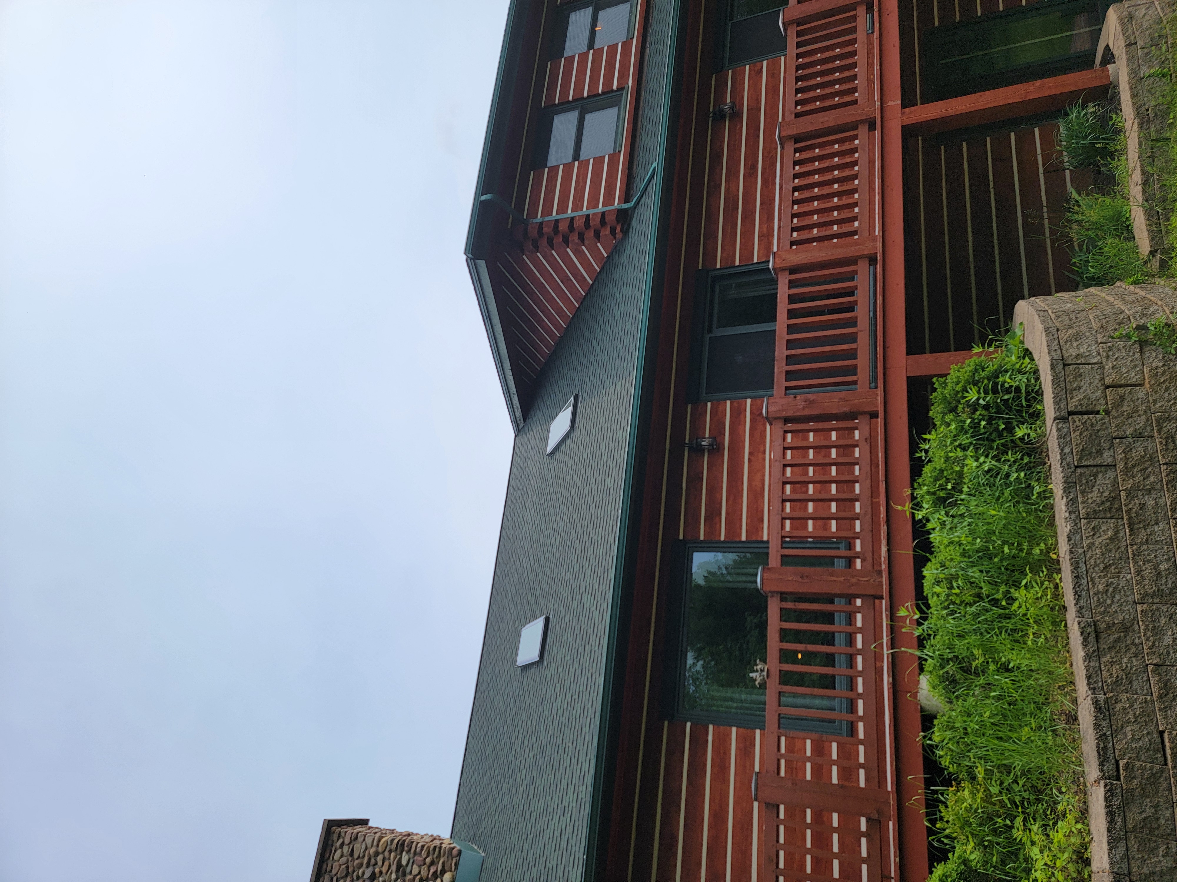 Rear view of a Mosinee, WI home with a new GAF Hunter Green roof, raised deck, and red outbuilding nearby.