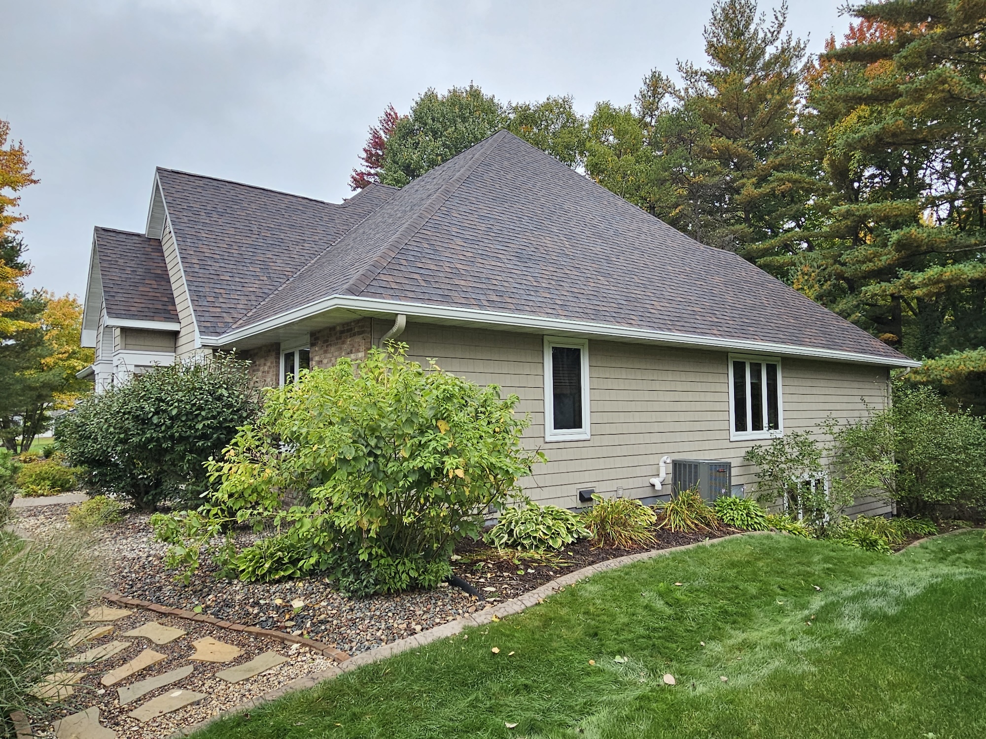 After roof replacement on a Wisconsin home showing the finished brown architectural shingle roof with brick, light siding, and white trim.