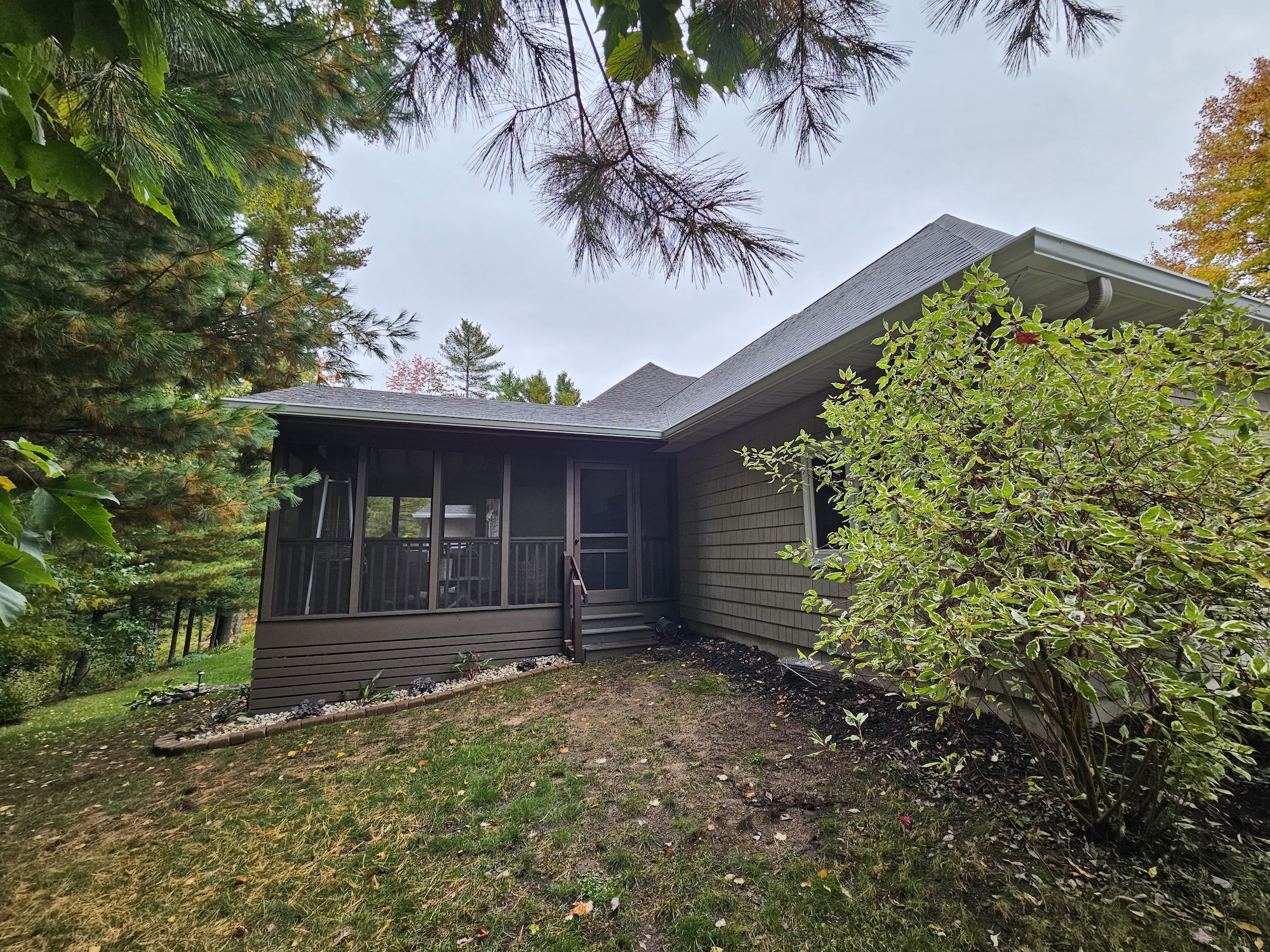 Back view of a Wisconsin home showing a brown architectural shingle roof over a screened porch and rear addition.